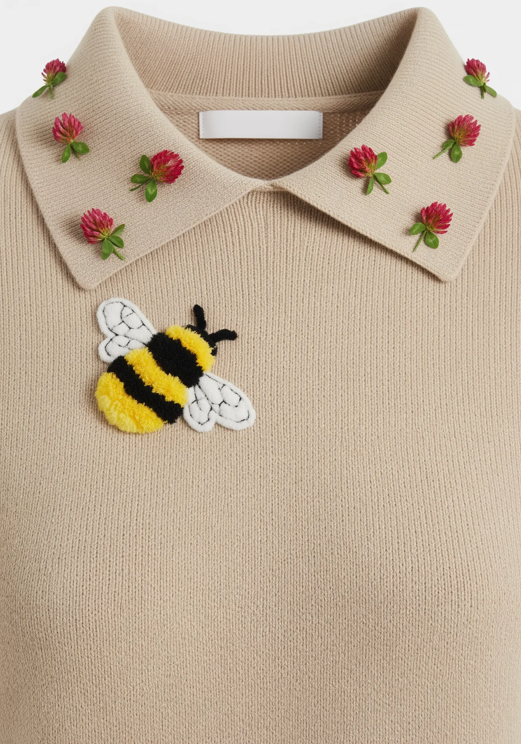 A fuzzy, 3D embroidered bee next to dimensional red clover flowers on a knit polo shirt.