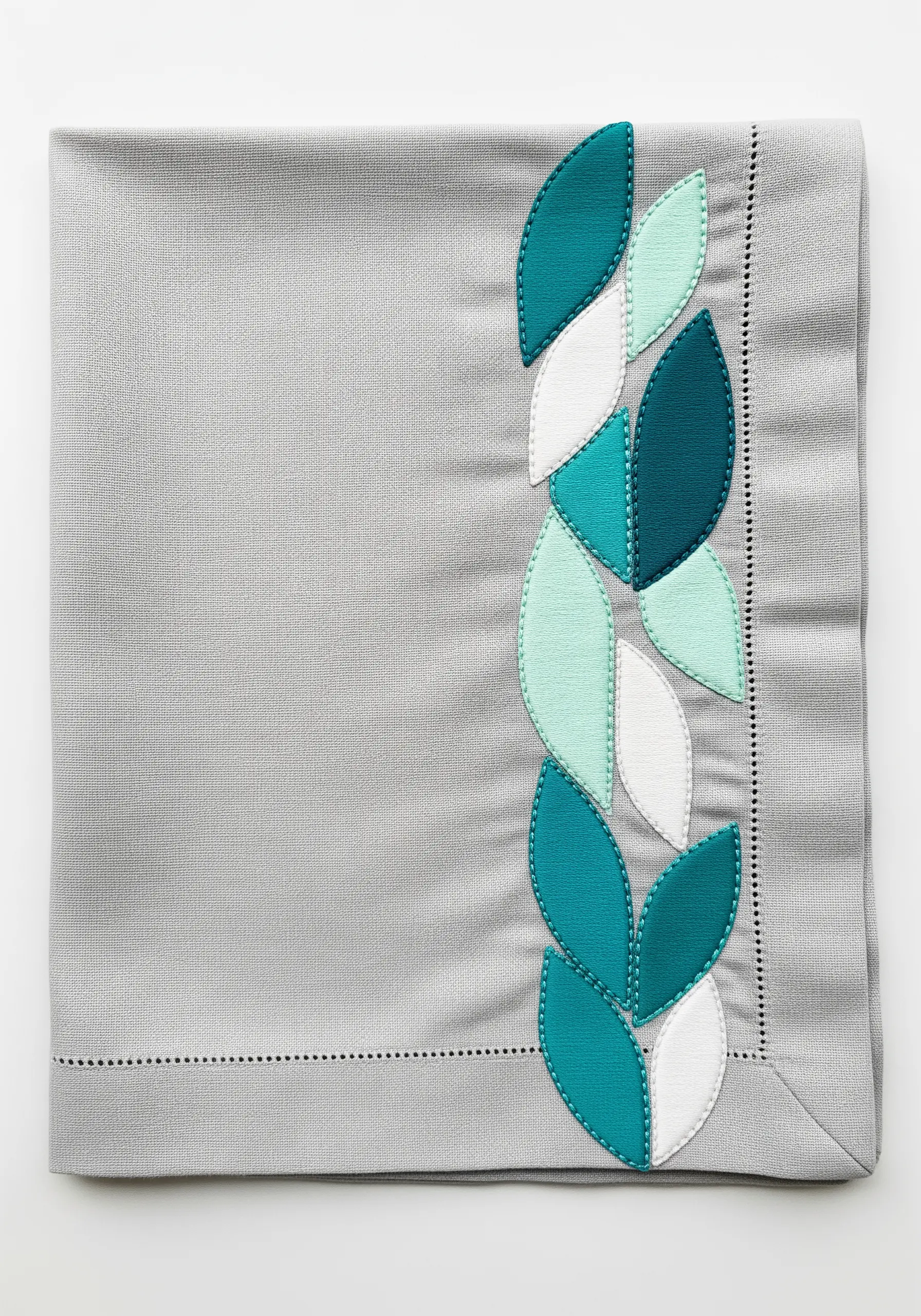 Modern leaf shapes in teal and white appliqué on a gray napkin.