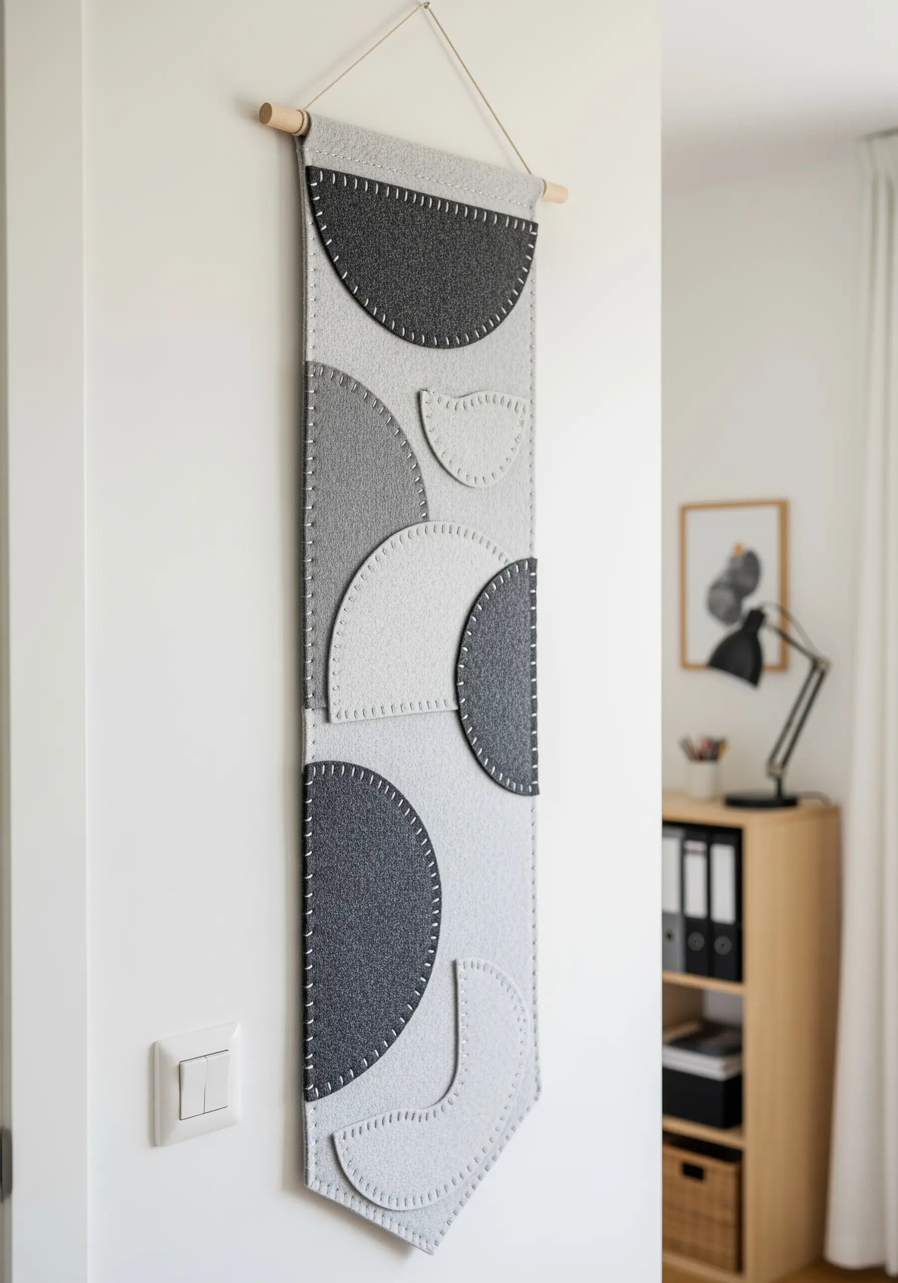 A narrow felt wall banner with layered geometric shapes in shades of grey.