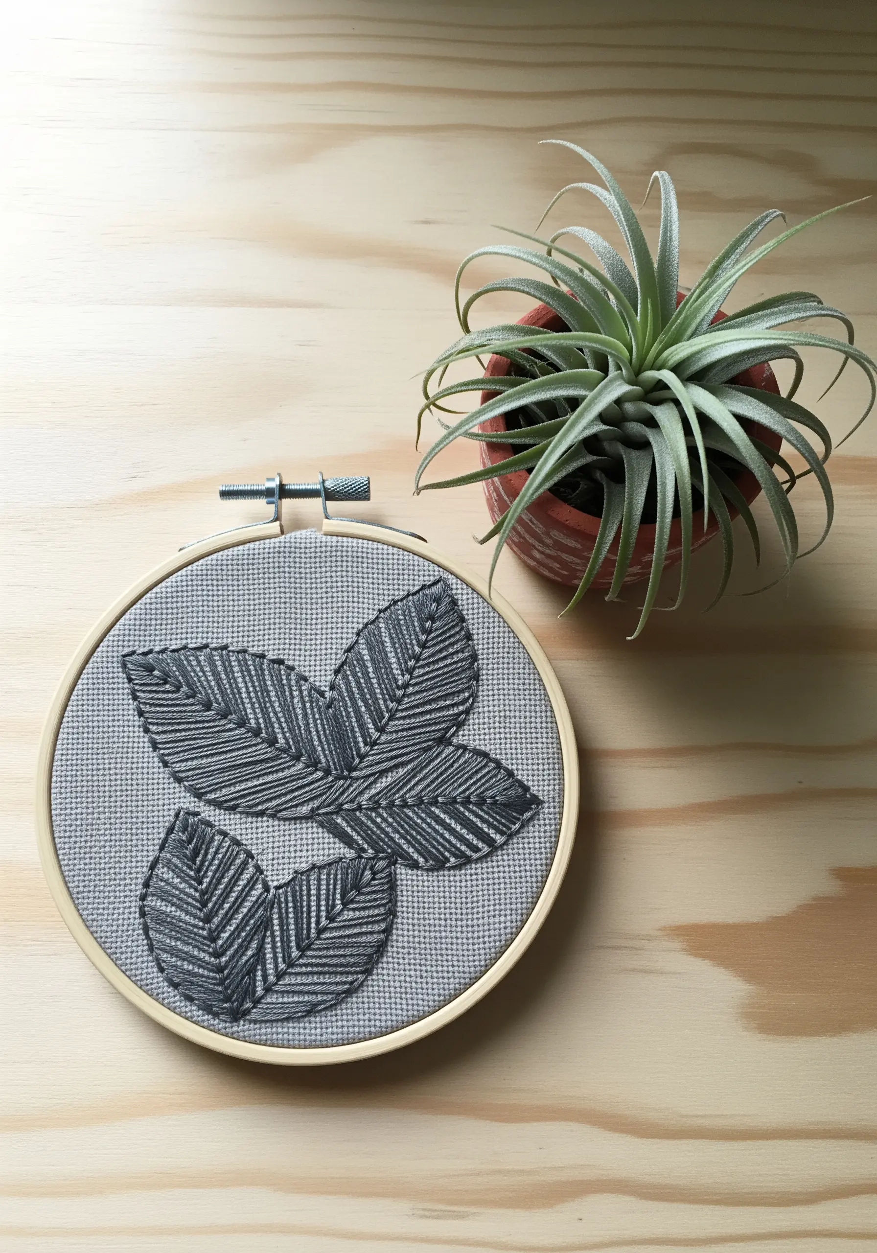 Three leaves embroidered in dark grey thread on a light grey fabric, showing textural fills.
