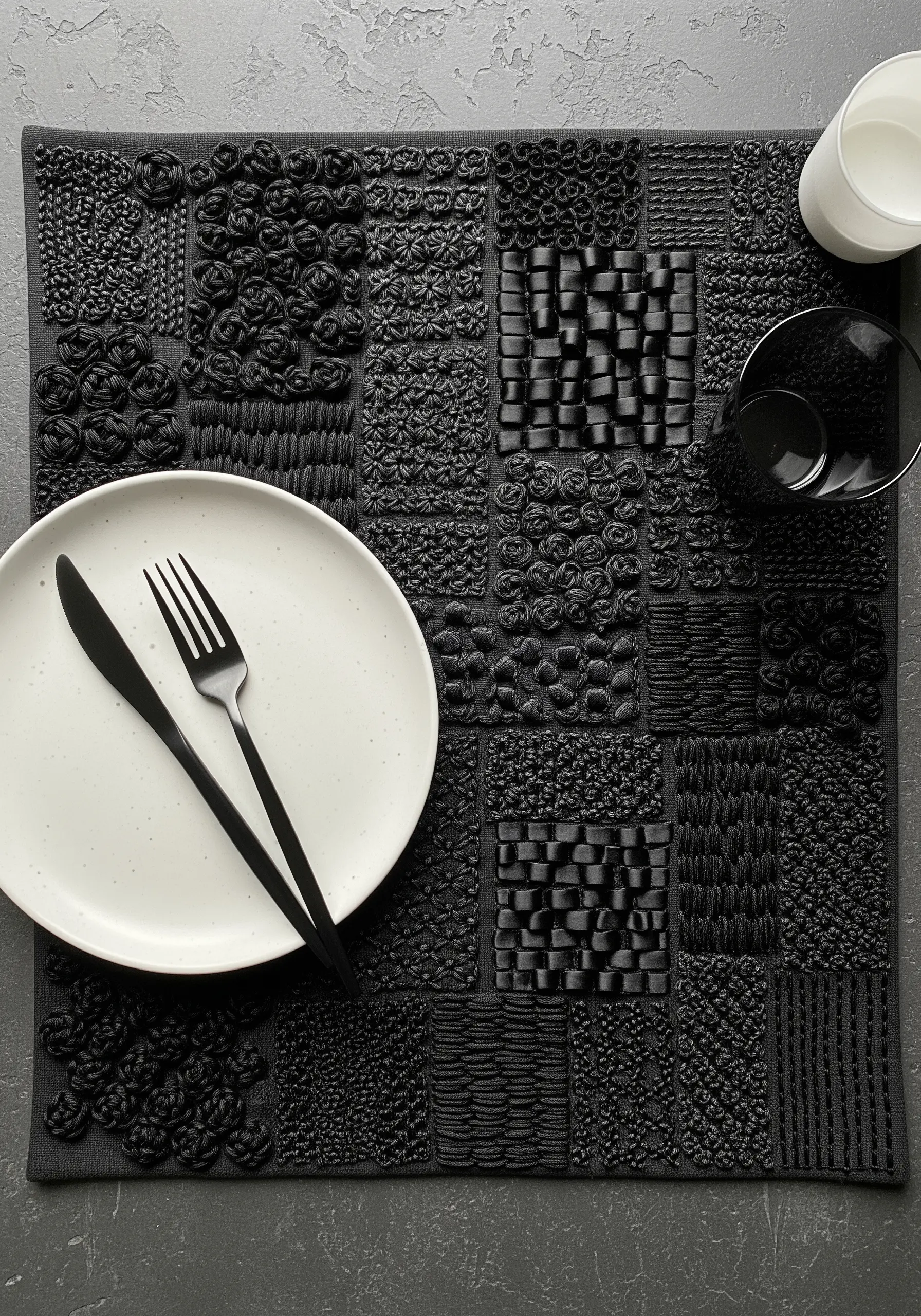 Black placemat with a grid of different high-texture black embroidery stitches