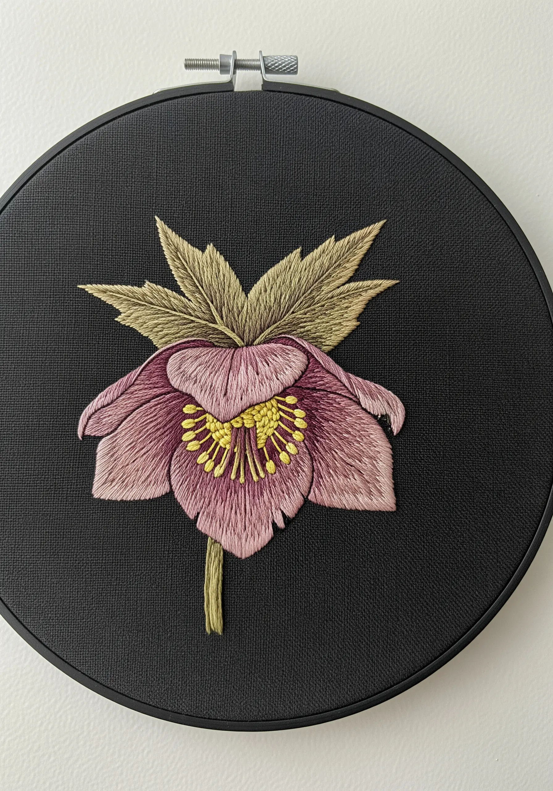 A thread-painted pink hellebore flower with yellow stamens on a black fabric background.