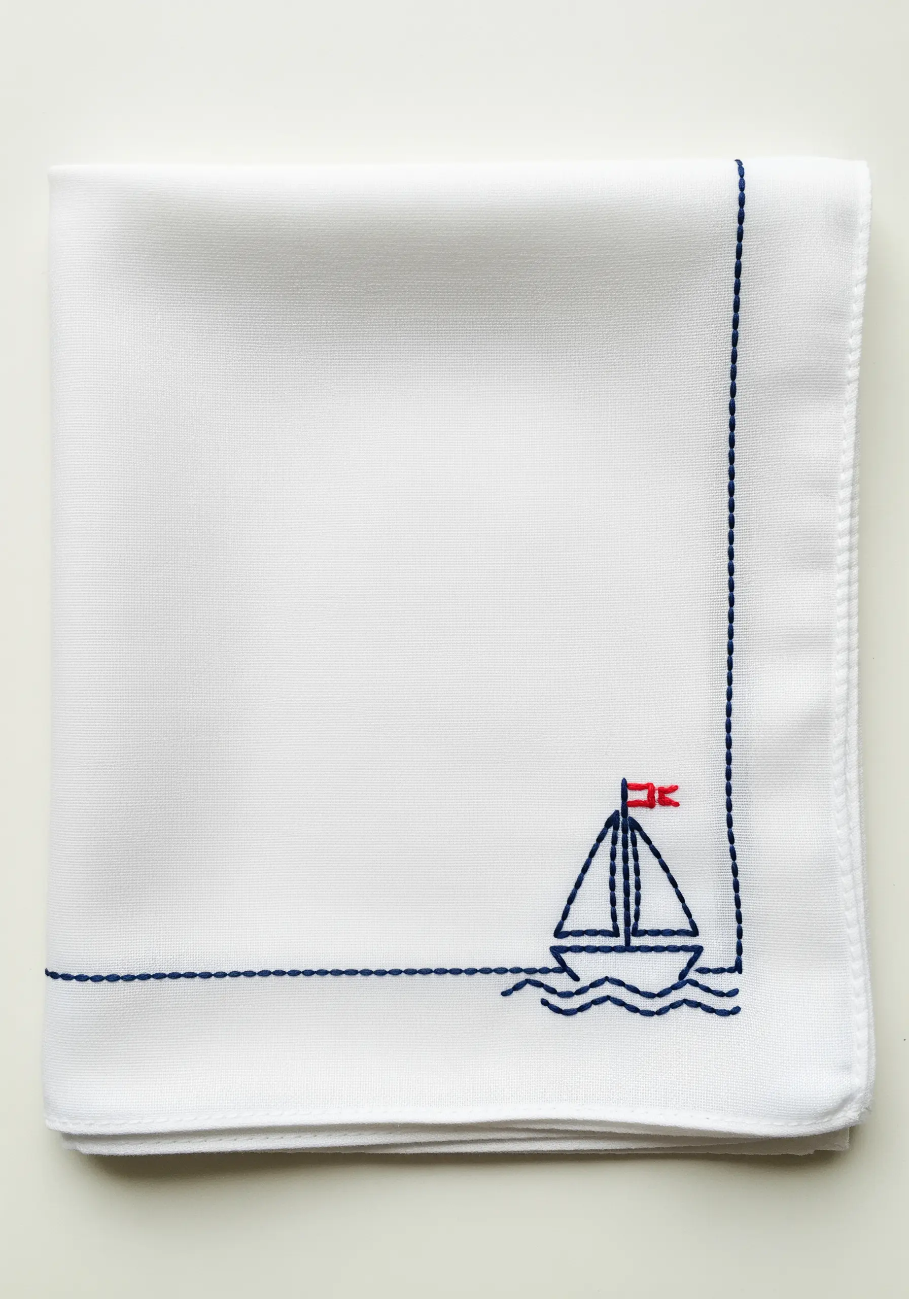 A minimalist sailboat integrated into the corner border of a white handkerchief.