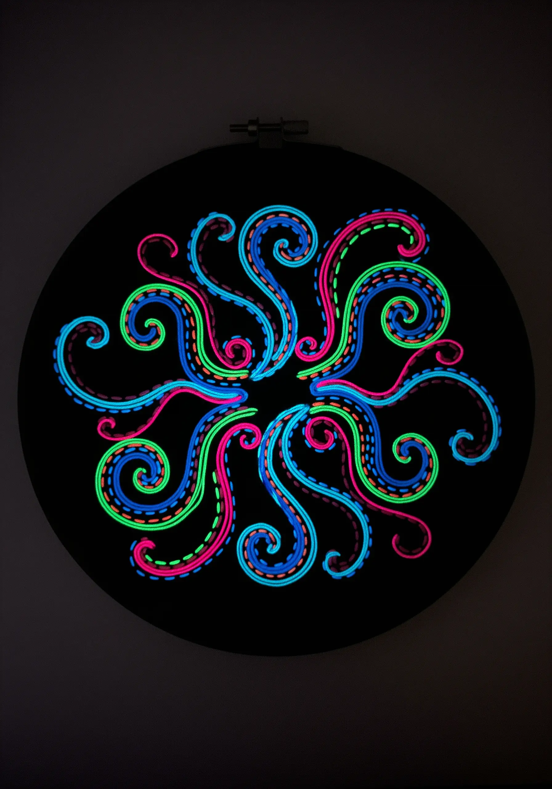 Glow-in-the-dark embroidery of a swirling neon mandala on a black background.