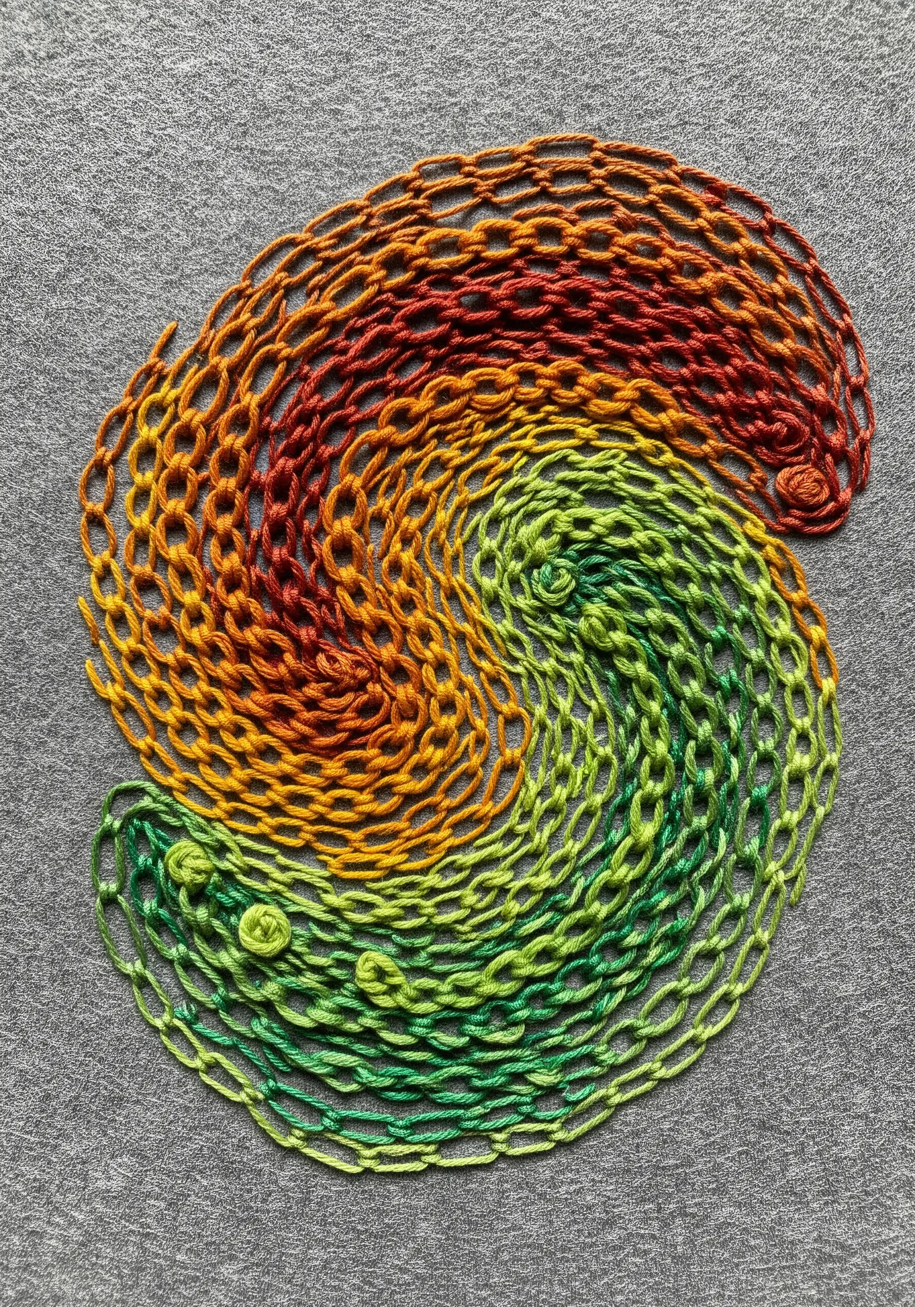 Interlocking swirls of open chain stitch in a red-to-green color gradient.