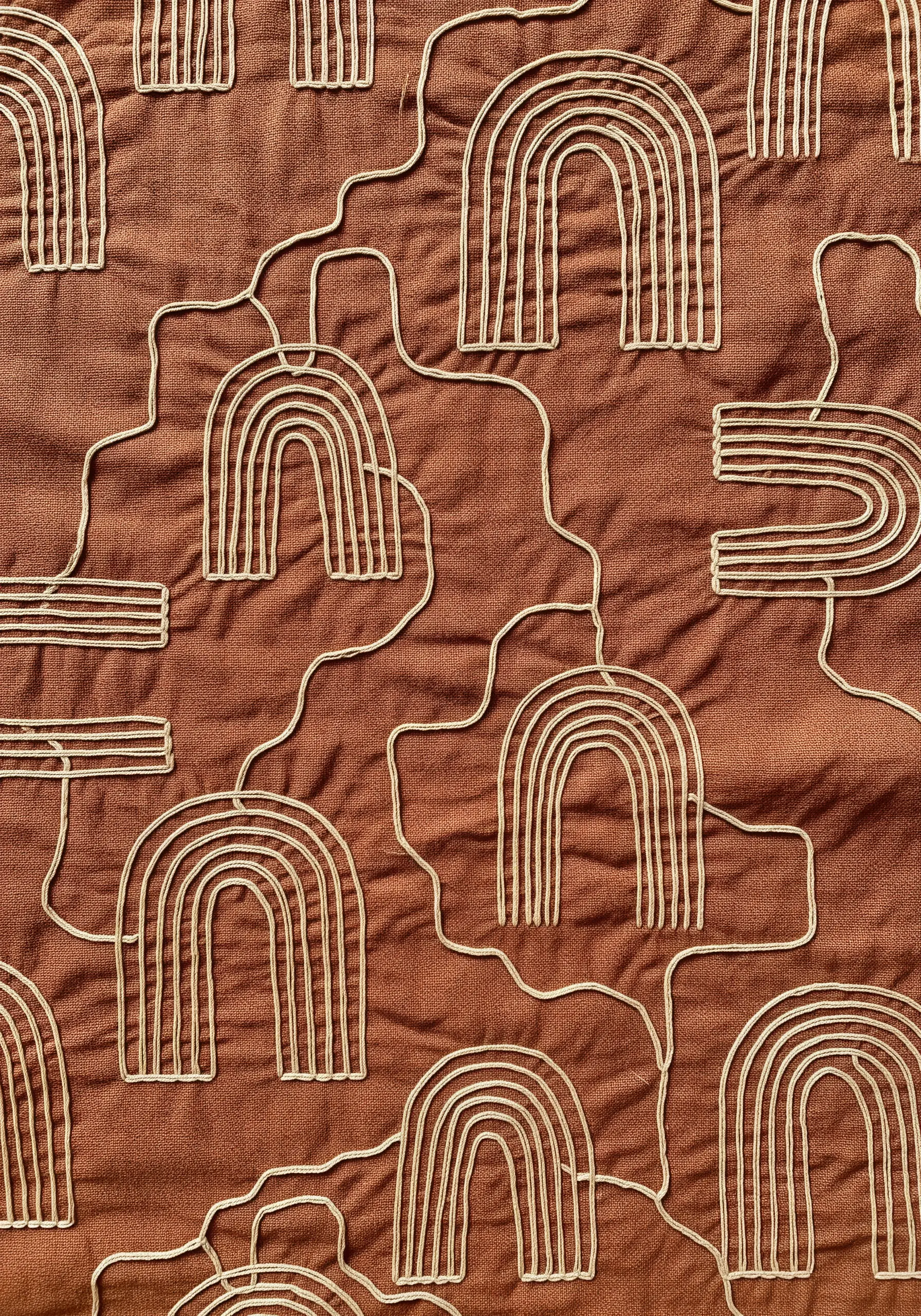 A textured pattern of embroidered arches connected by meandering lines on terracotta fabric.