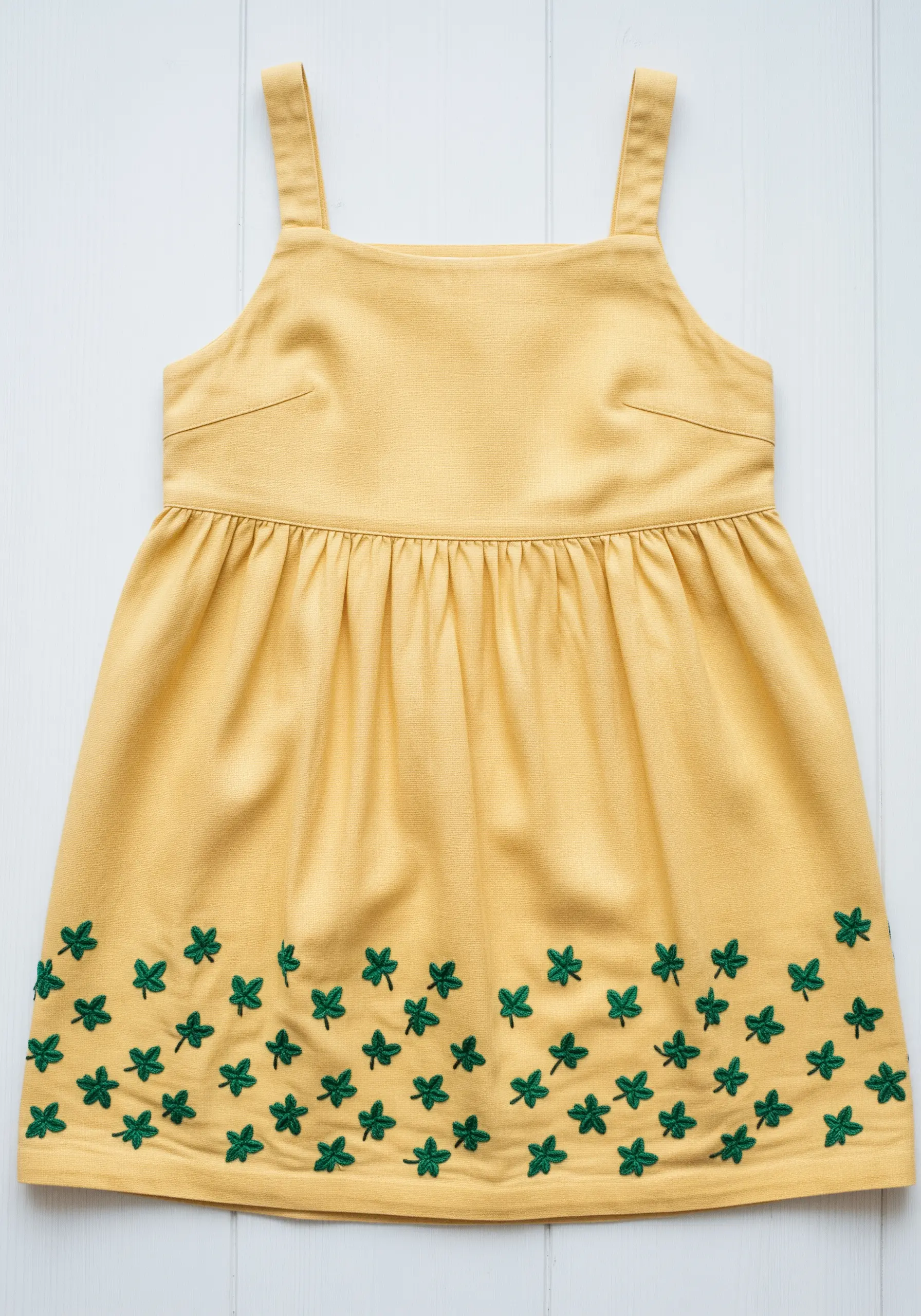 A scattered border of green ivy leaf clusters embroidered along the hem of a yellow dress.