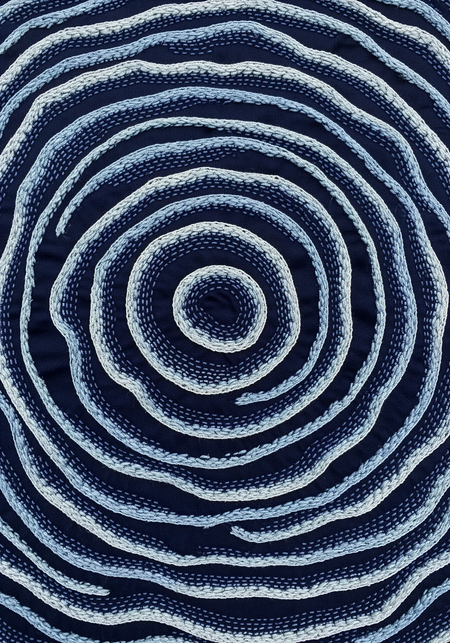 Organic, irregular concentric circles in blue and white using whipped running stitch.