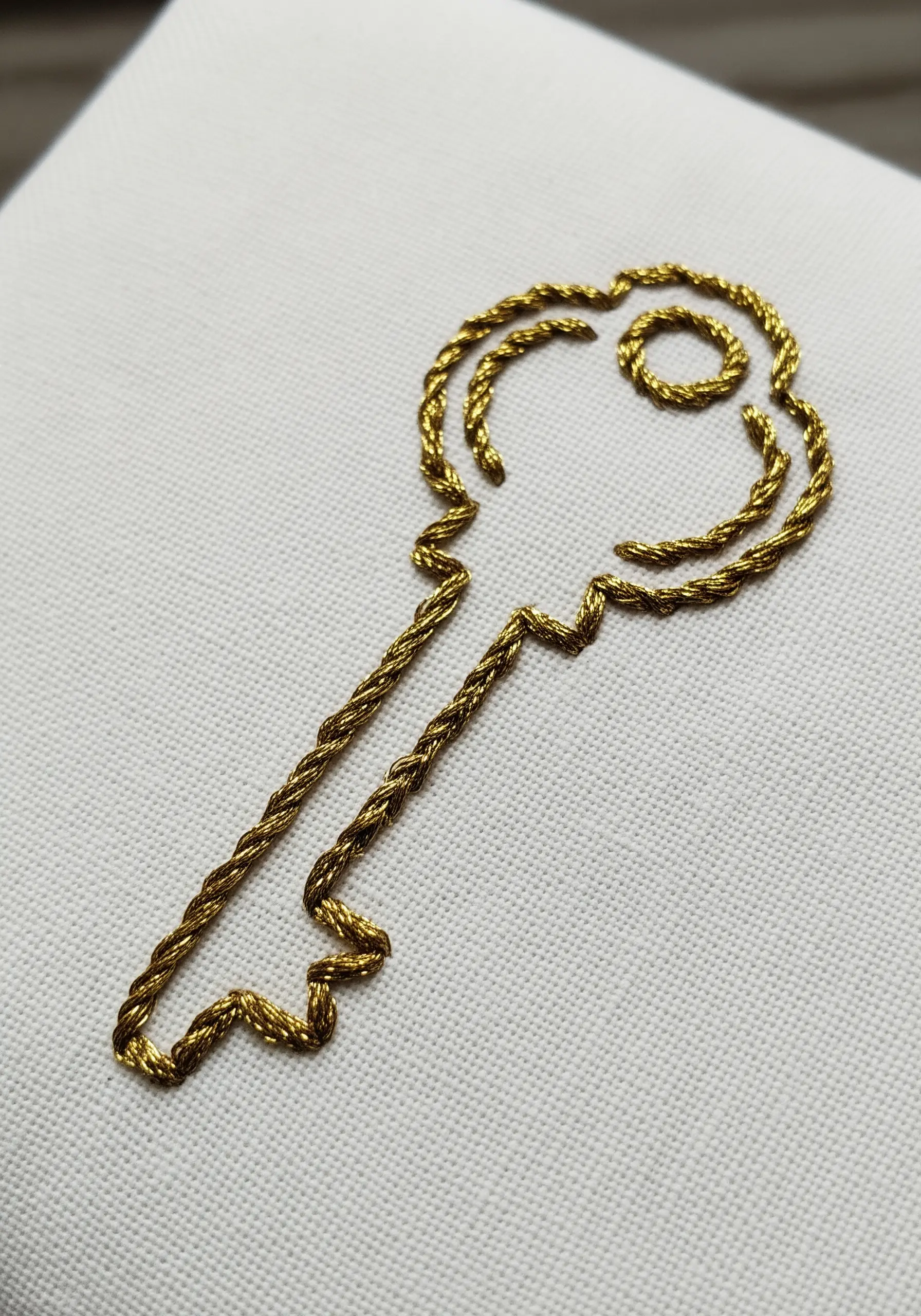 A golden key outlined with a decorative, textured chain stitch.