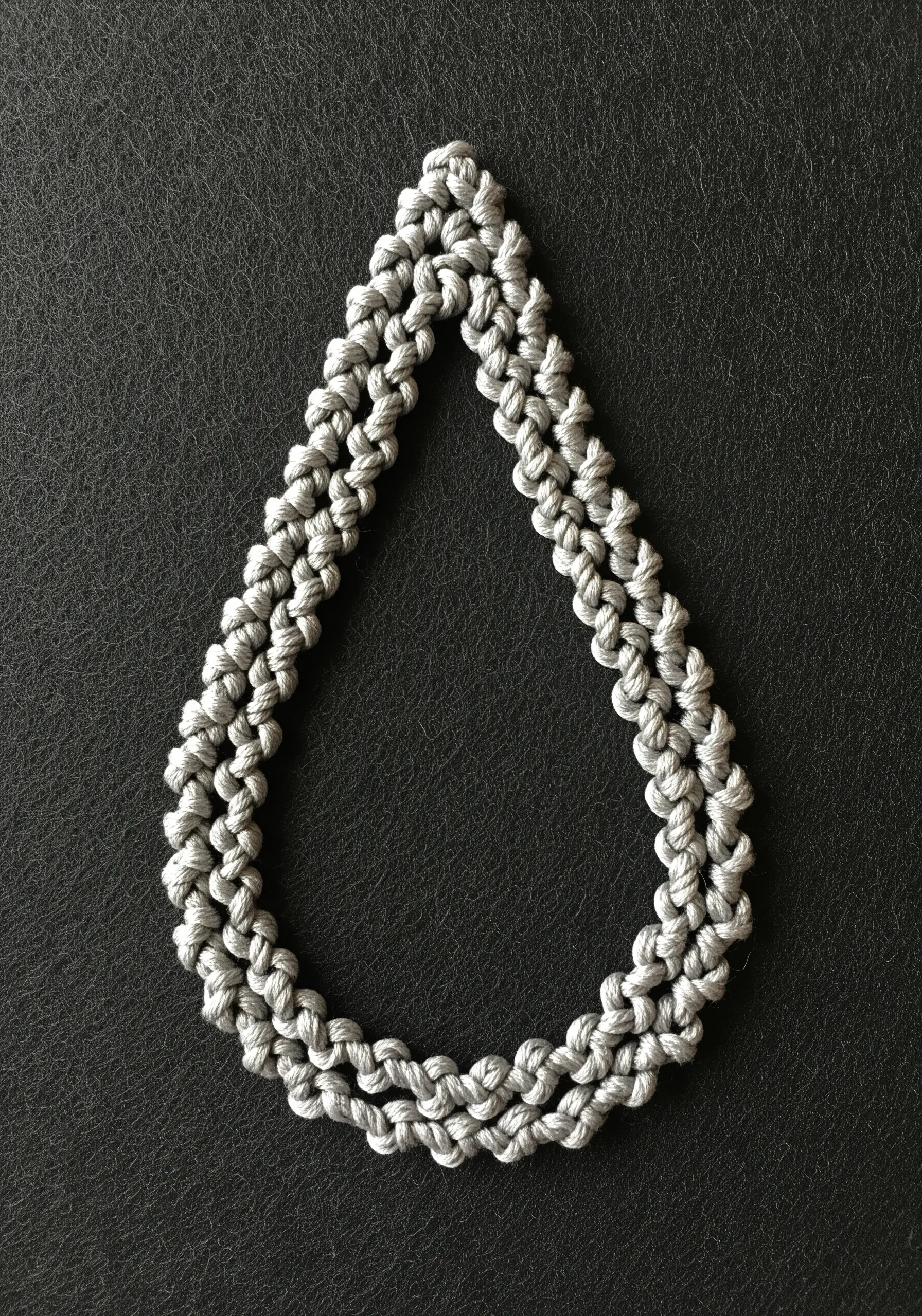 A teardrop shape outlined with a double row of grey, textured Palestrina knots on black leather.