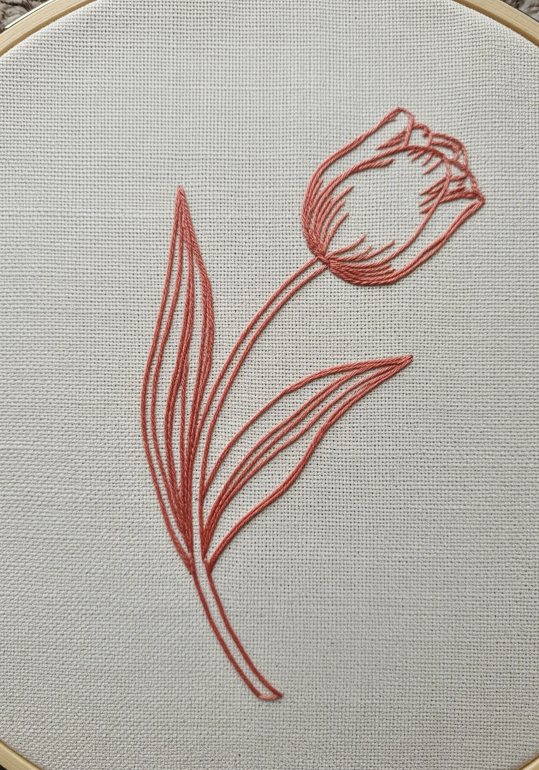 A line art tulip embroidered in a single coral color on Aida cloth.