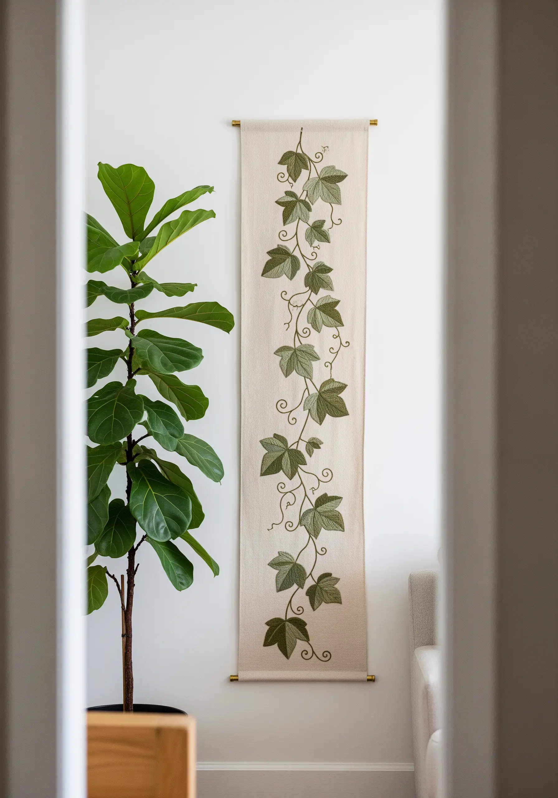 A narrow wall hanging with an embroidered green ivy vine climbing up the neutral fabric.