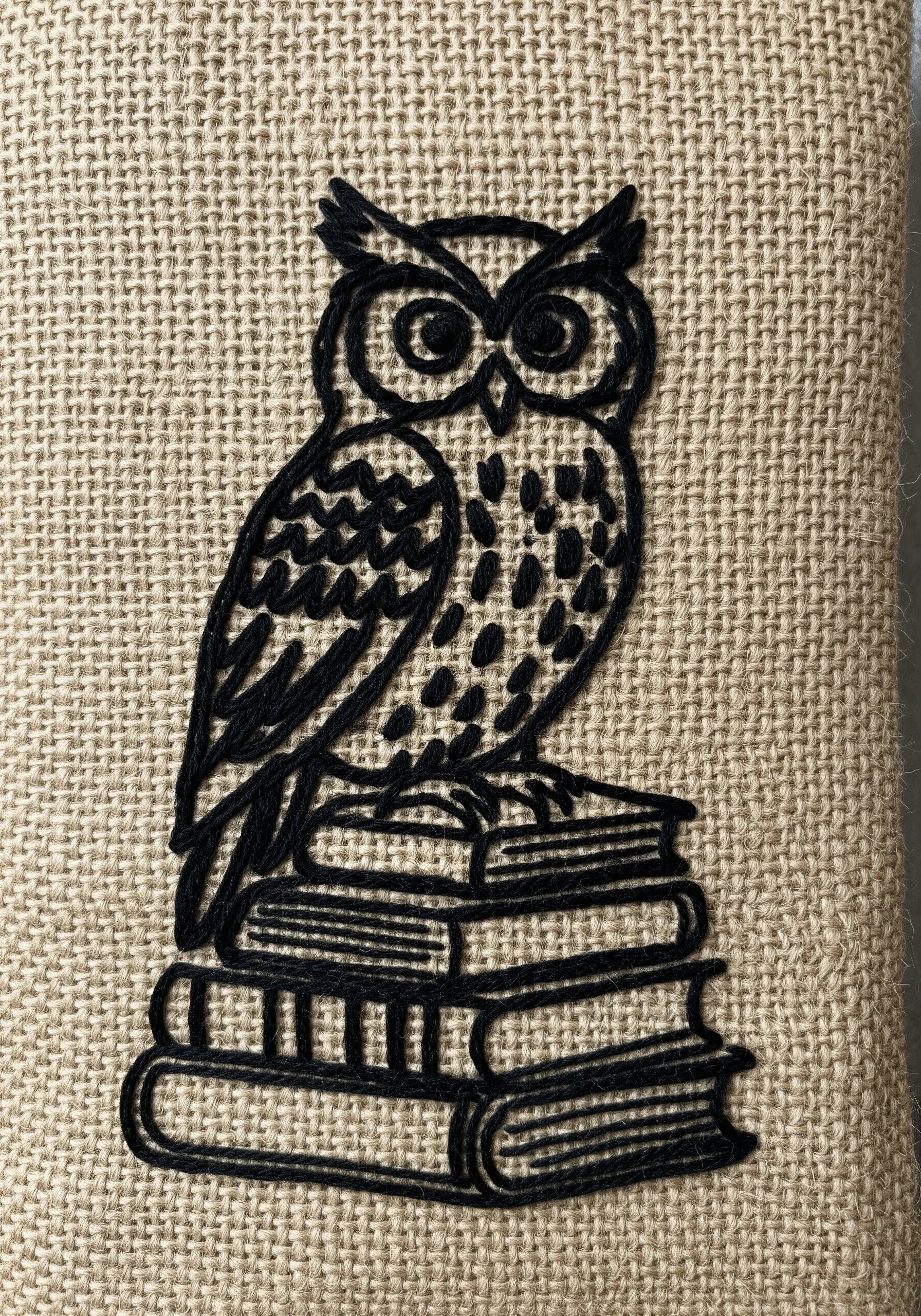 Black owl embroidery on a stack of books on textured beige burlap
