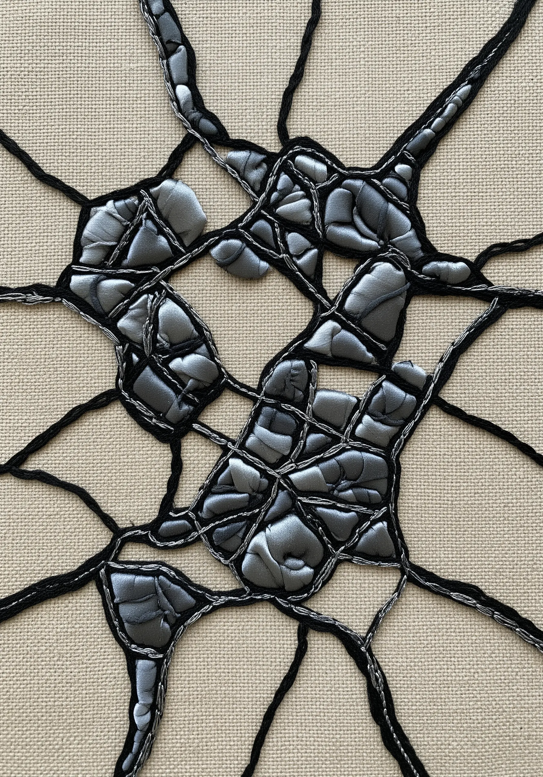 Abstract cracked texture made with padded silver satin appliqué outlined in black and silver thread.