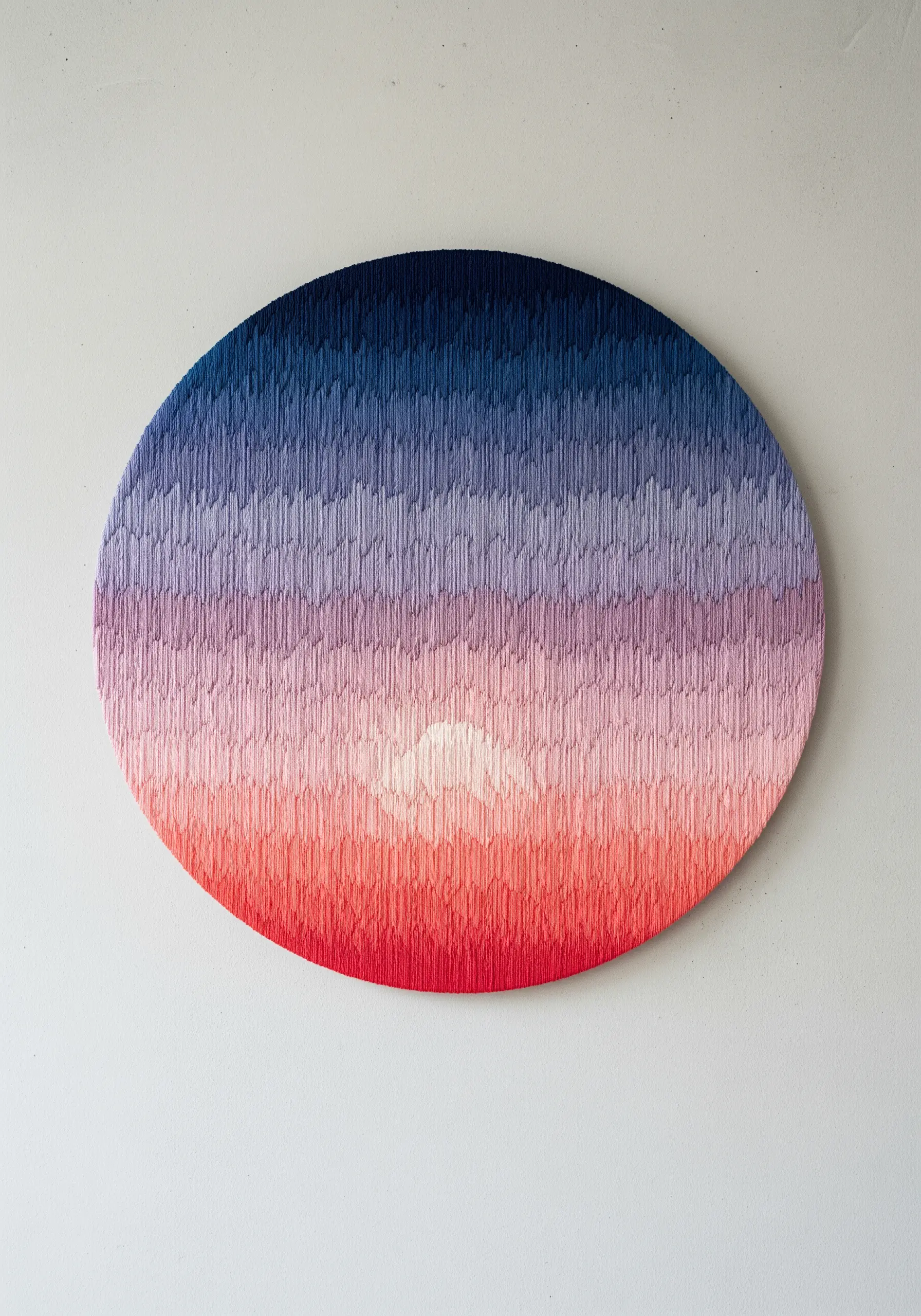 A round embroidery canvas filled with a vertical stitch gradient from dark blue to pink and red.