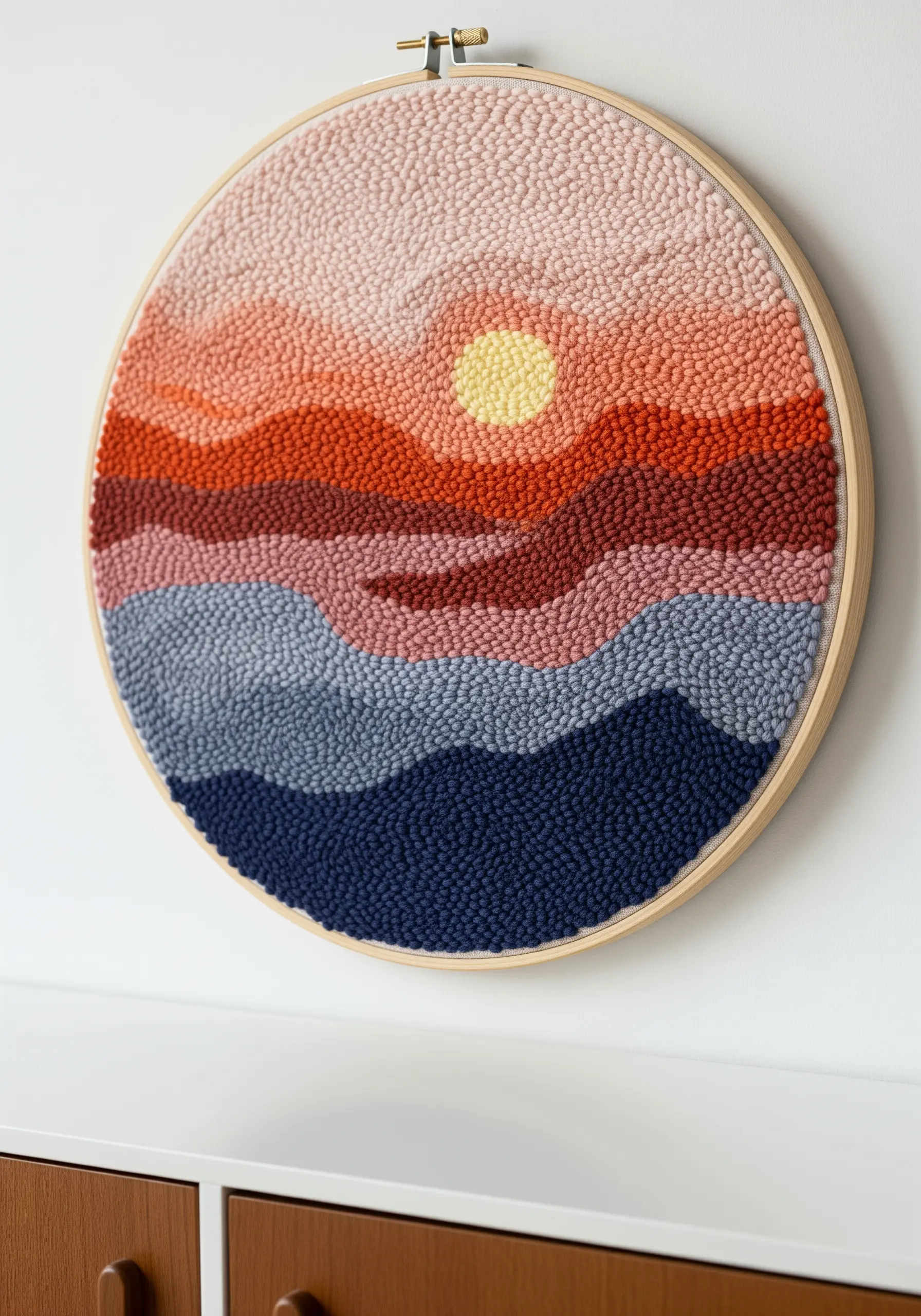 Punch needle embroidery of a sunset over rolling hills in a wooden hoop.