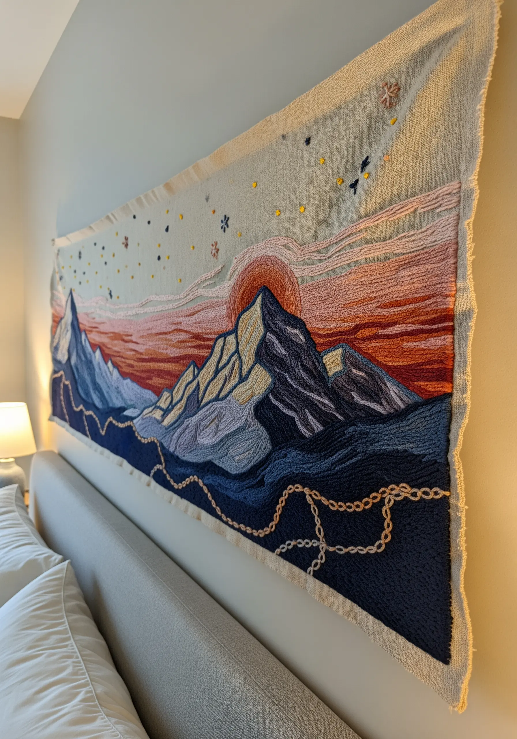 Large embroidered tapestry of a mountain range at sunset hanging above a bed.