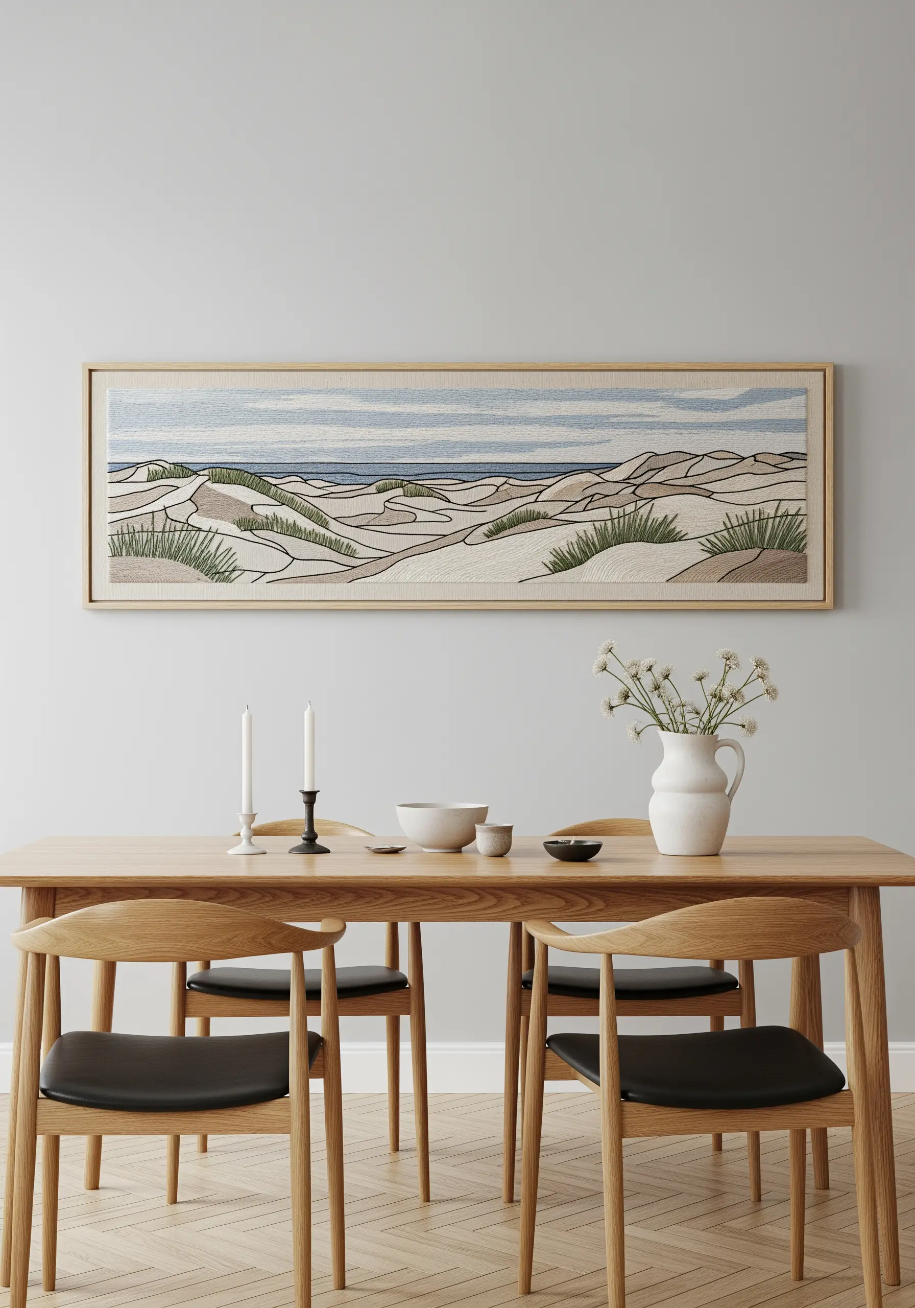 A panoramic framed embroidery of sand dunes with sparse grasses above a dining table