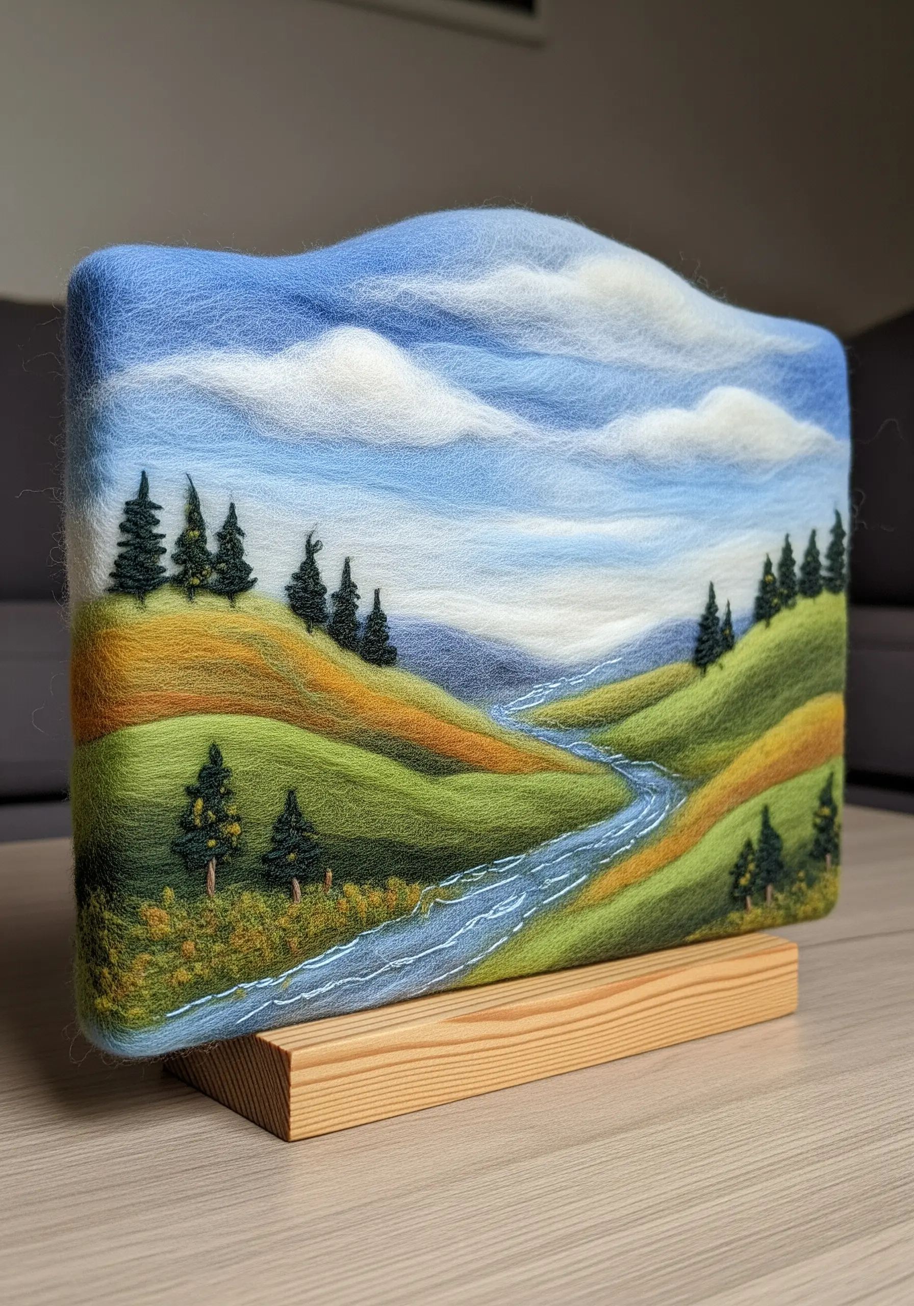 A serene landscape of rolling hills and a river, created with needle-felted wool.