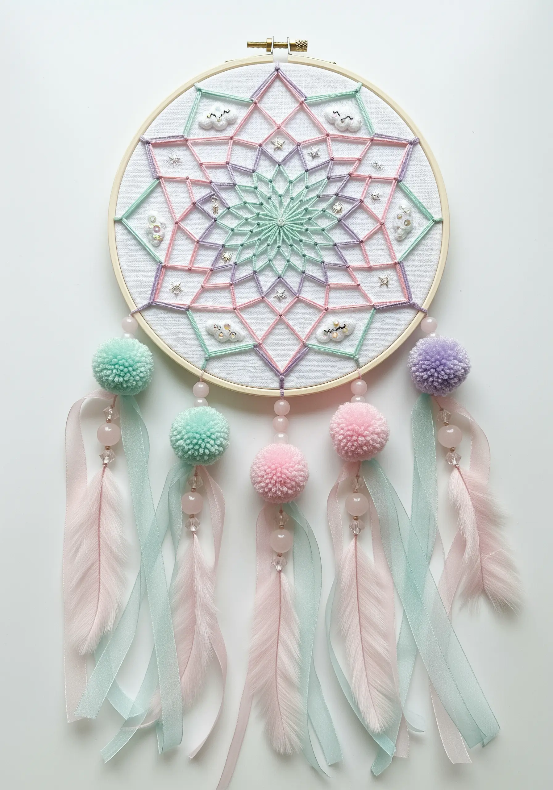 Pastel rainbow string art dreamcatcher with pom-poms, ribbons, and feathers.