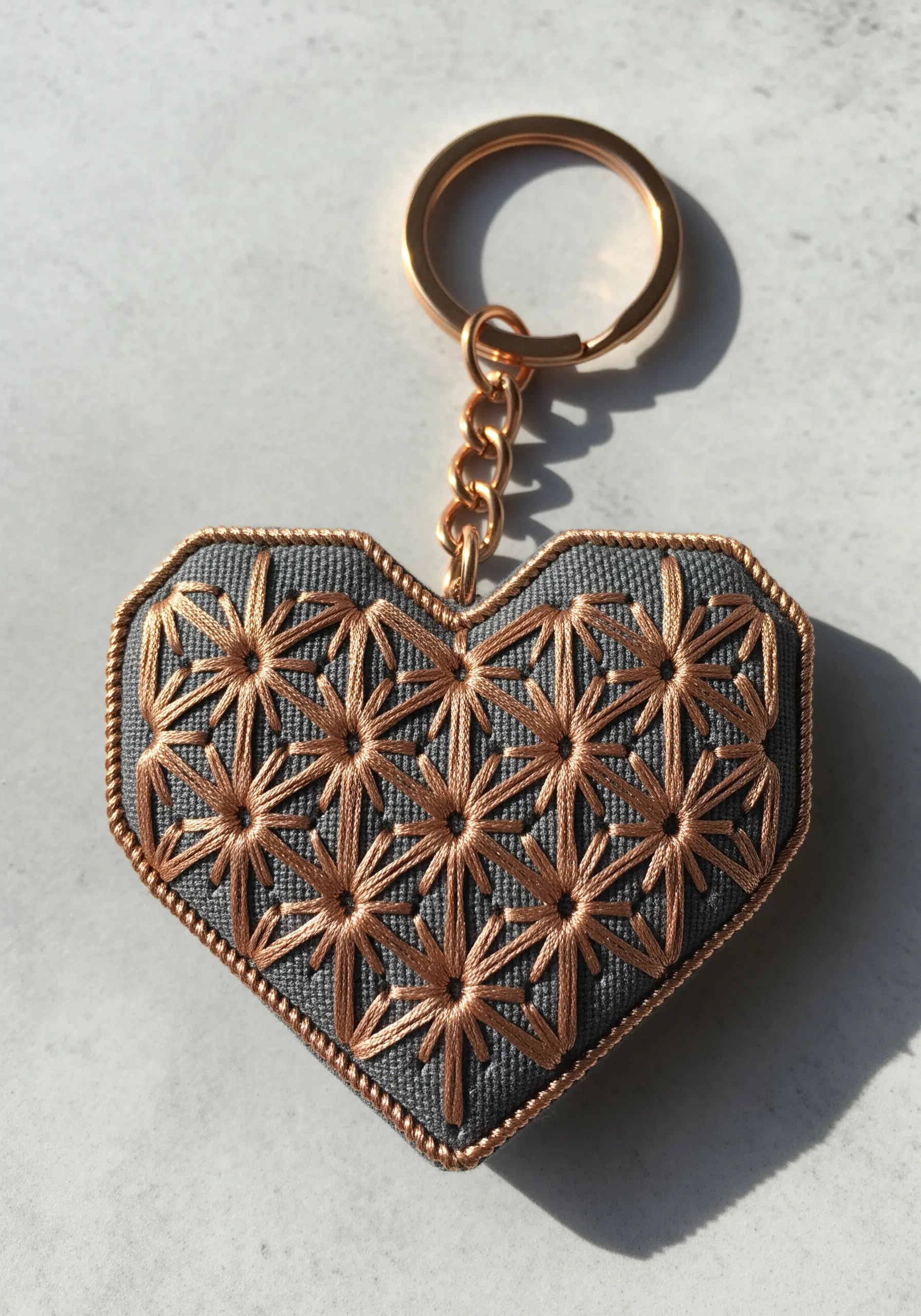 Heart-shaped keychain filled with a geometric pattern of radiating bronze stitches