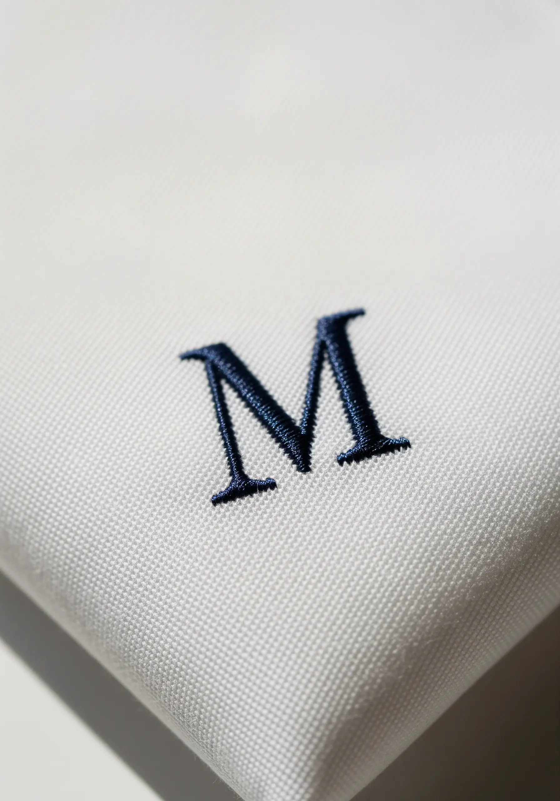 A classic navy blue serif letter 'M' flawlessly embroidered on a crisp white handkerchief.