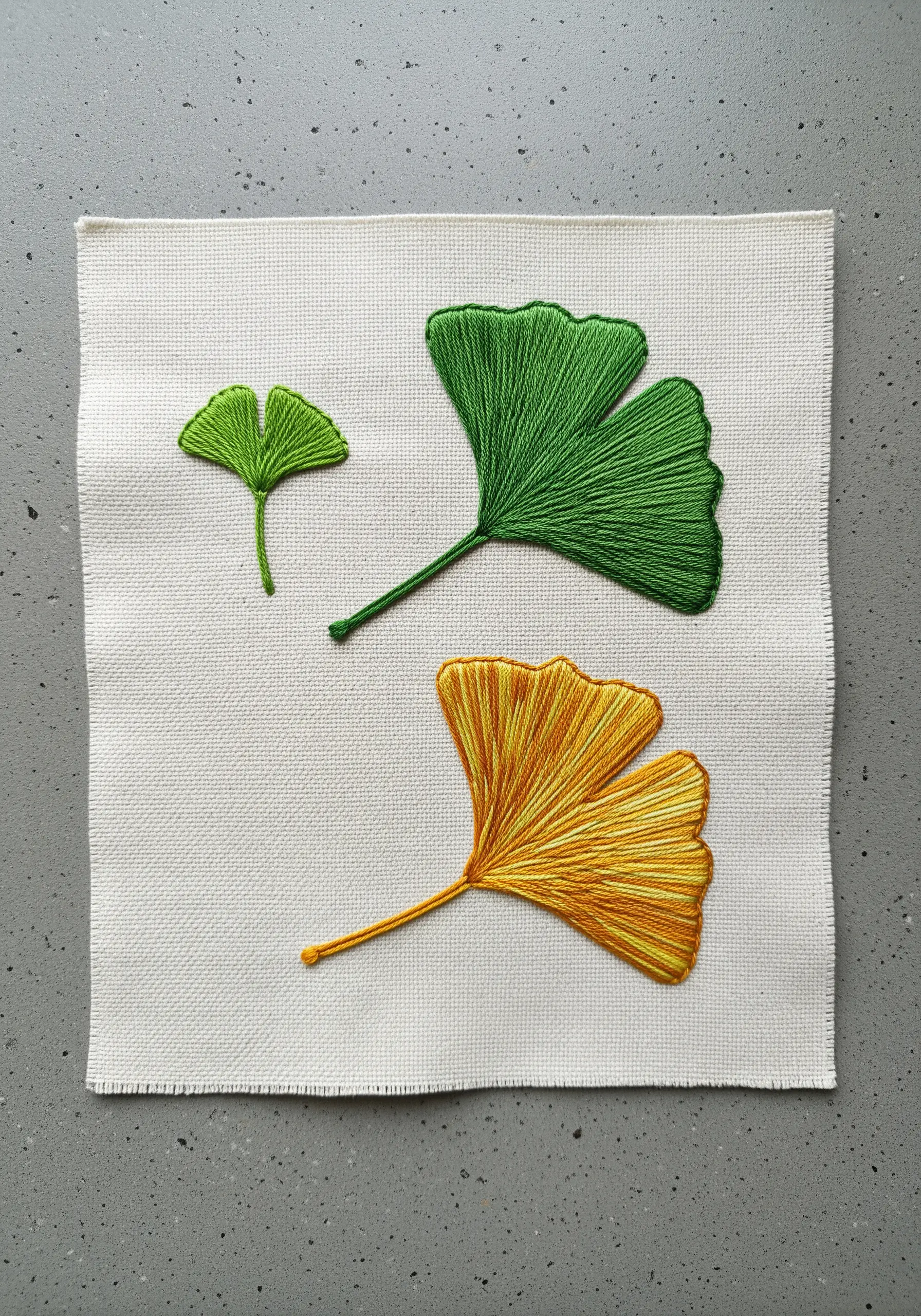 Three embroidered ginkgo leaves in green and yellow, showcasing a smooth satin stitch.