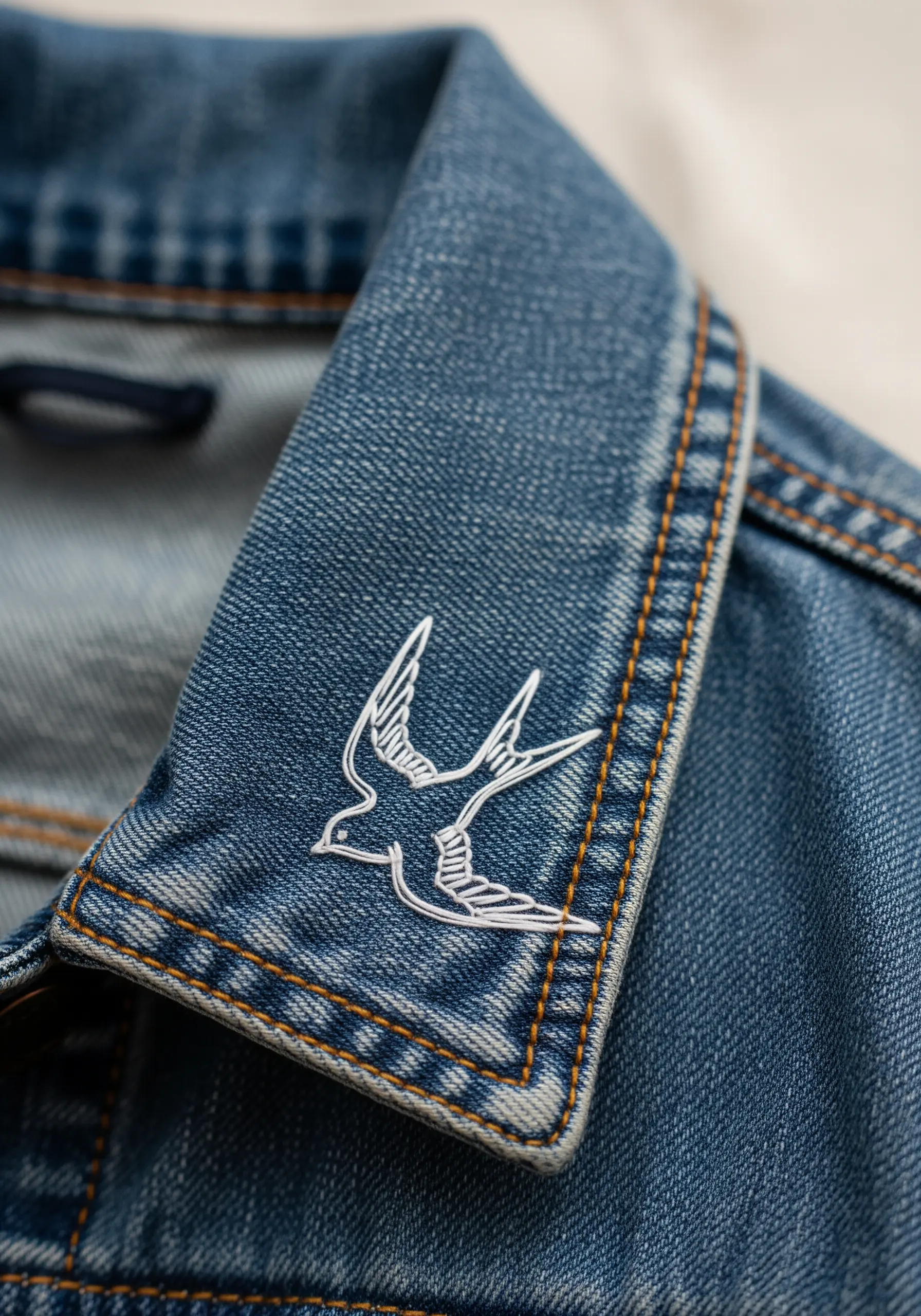 A delicate white swallow embroidered on the collar of a denim jacket.