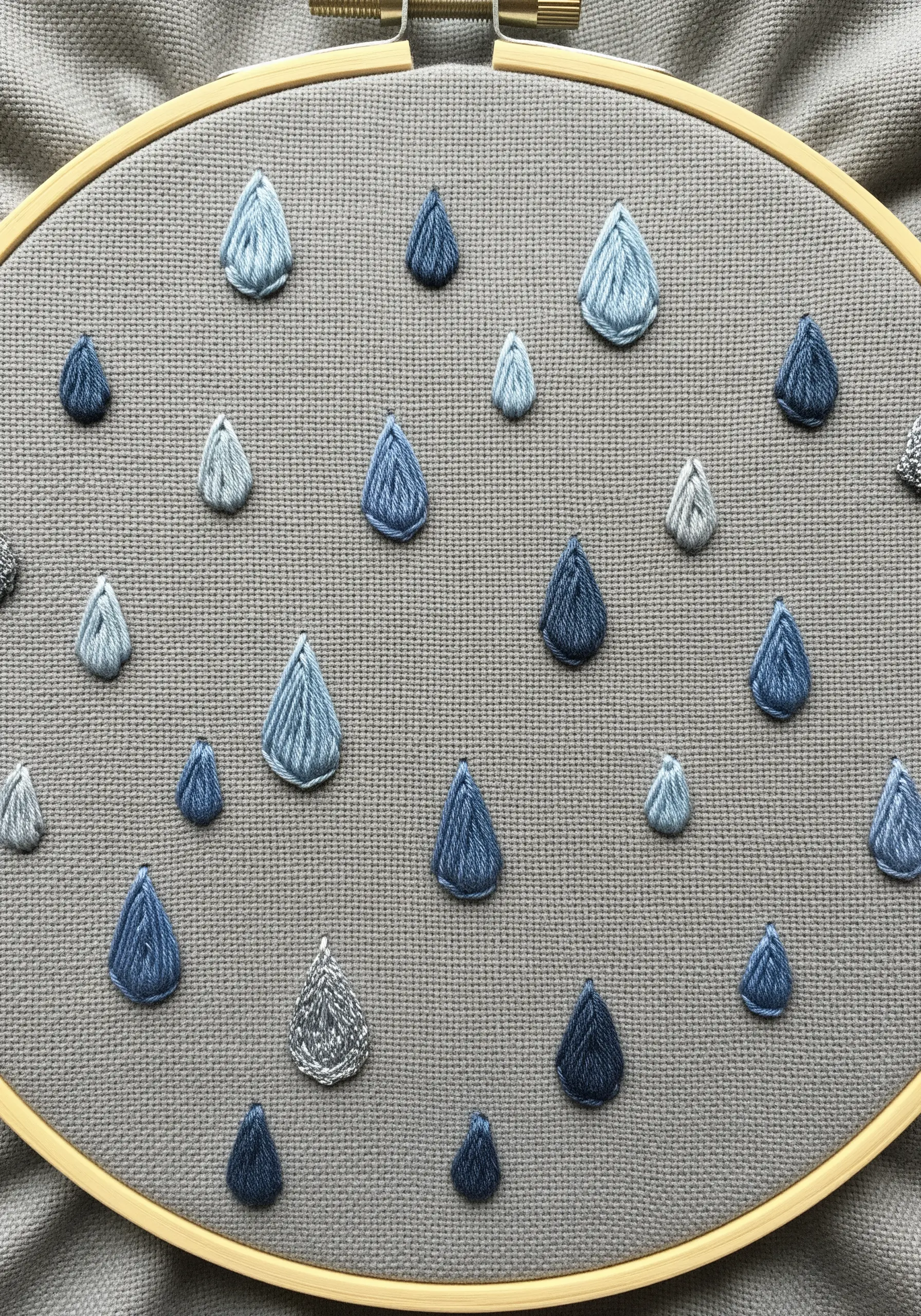 Satin-stitched raindrops in various shades of blue and silver scattered across gray fabric.