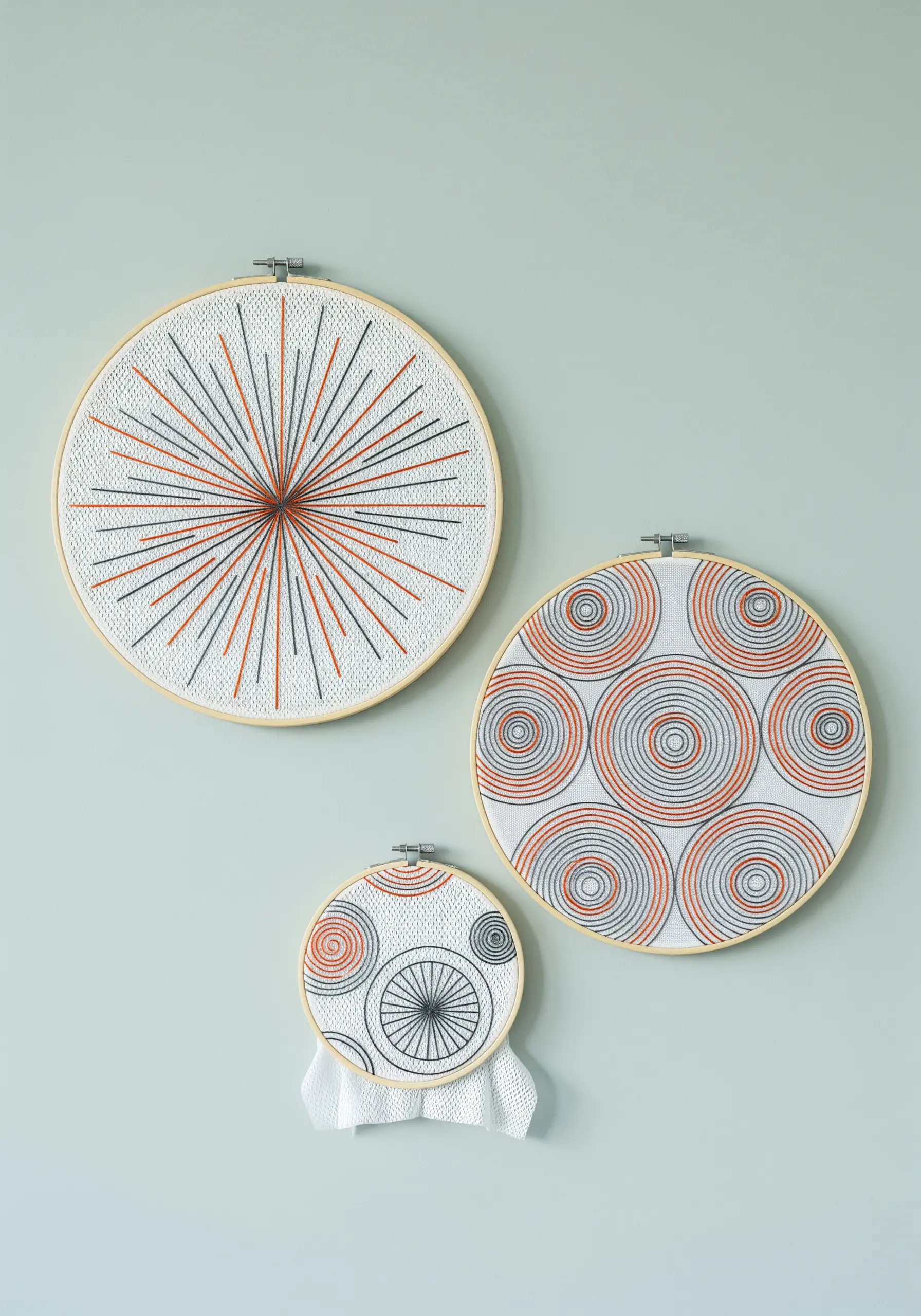 Three embroidery hoops with op-art designs of circles and lines in black, white, and orange.
