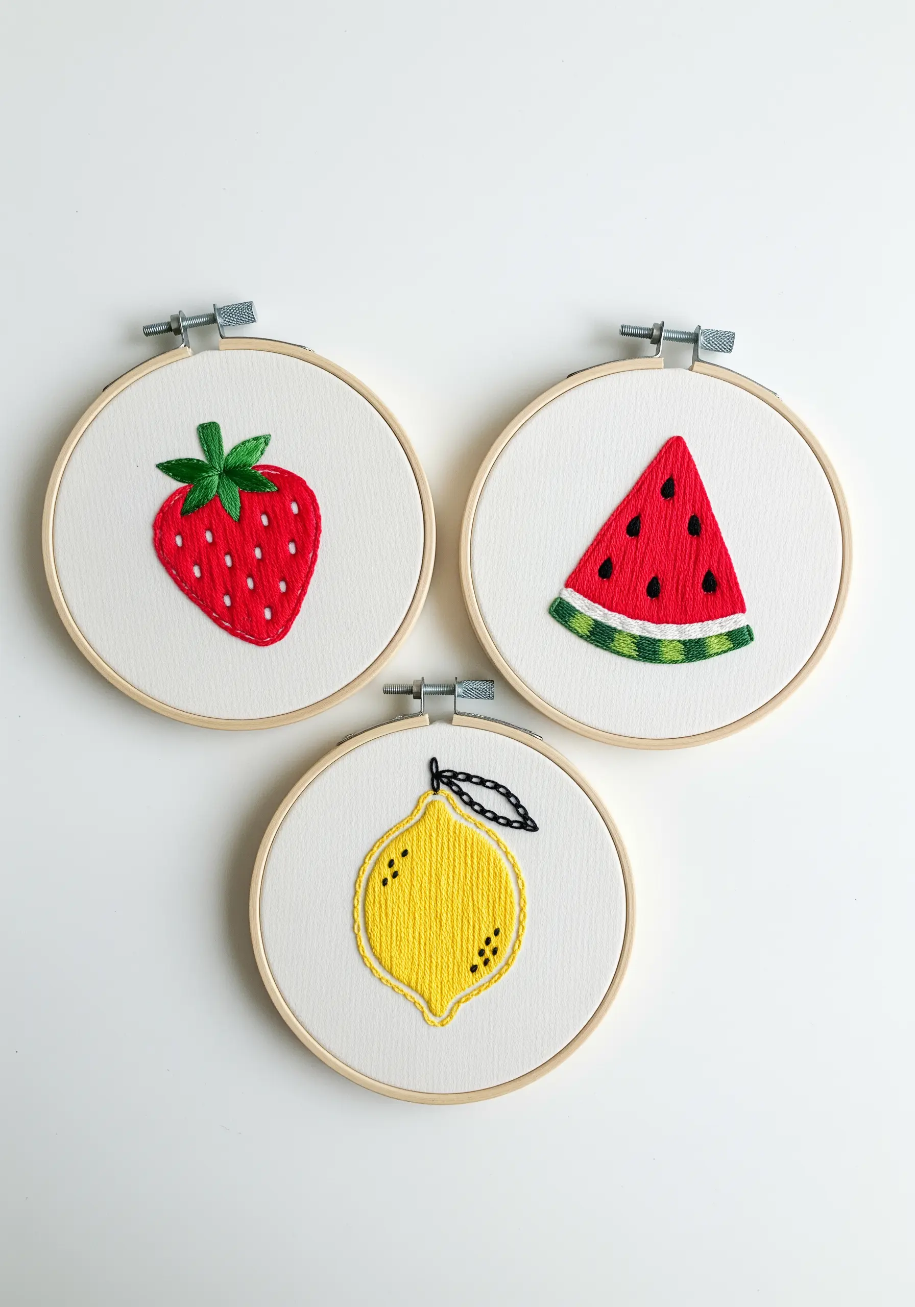 Three embroidery hoops featuring a strawberry, watermelon, and lemon with clean satin stitches.