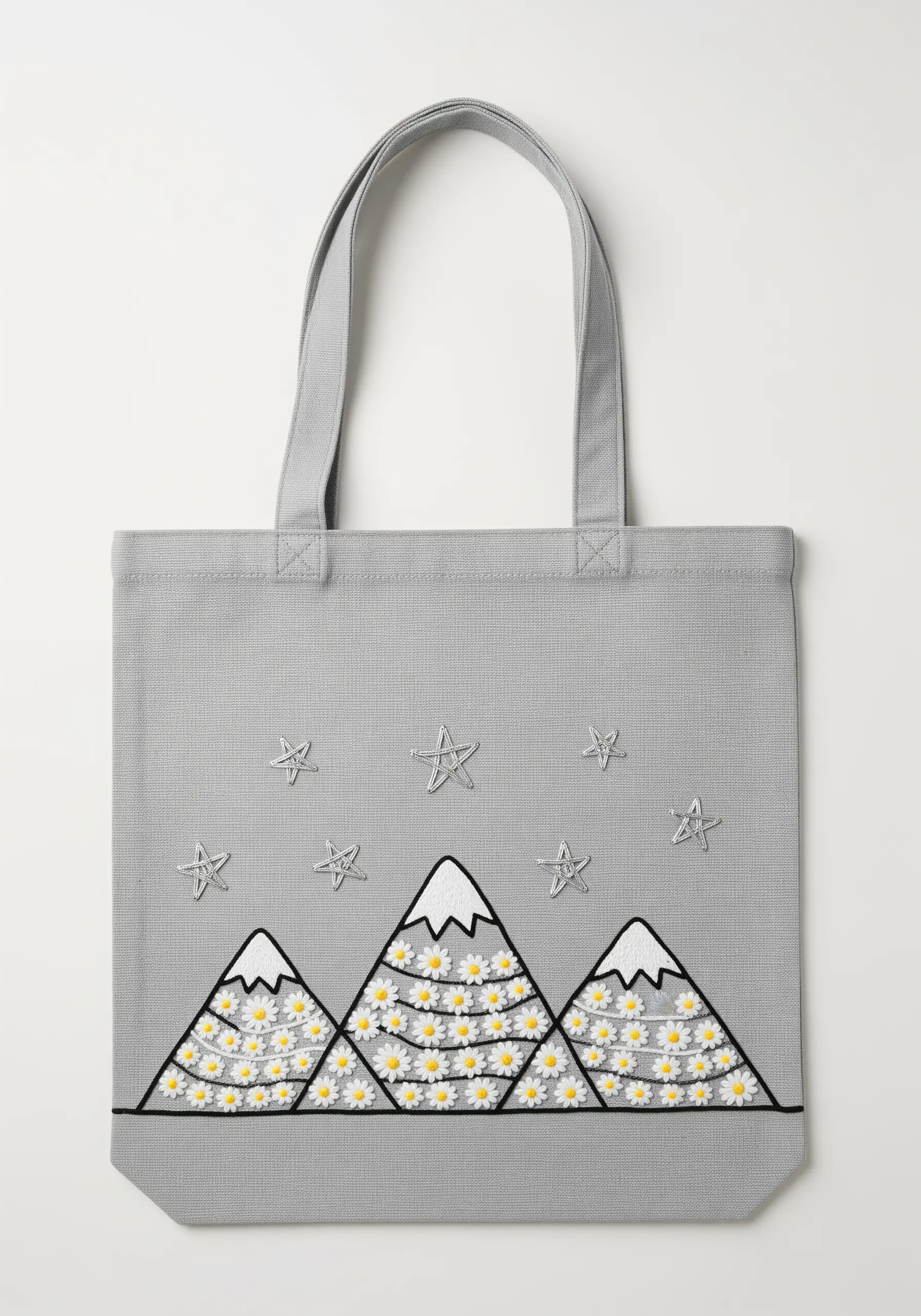 Graphic mountains filled with tiny embroidered daisies on a light gray tote bag.