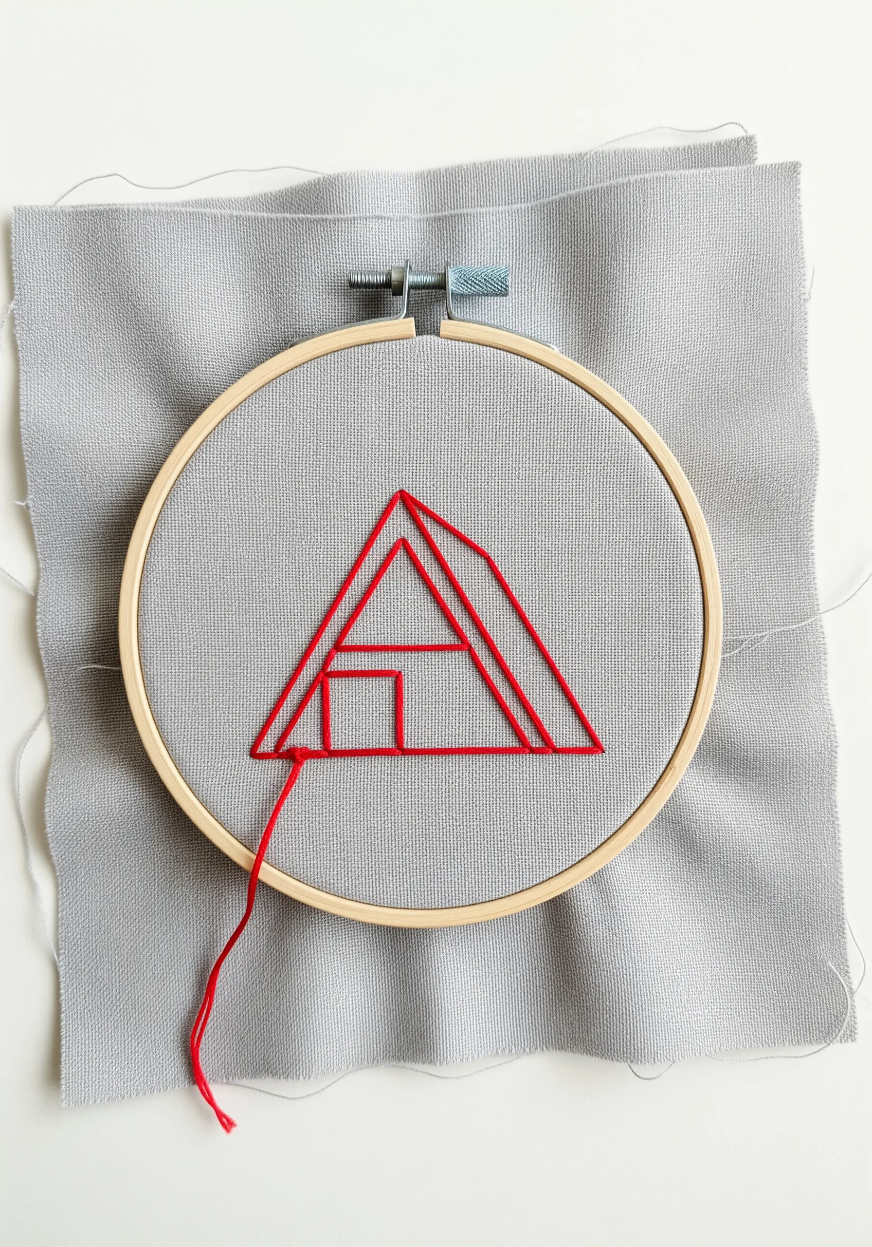 A minimalist geometric house outline in red thread on gray fabric.