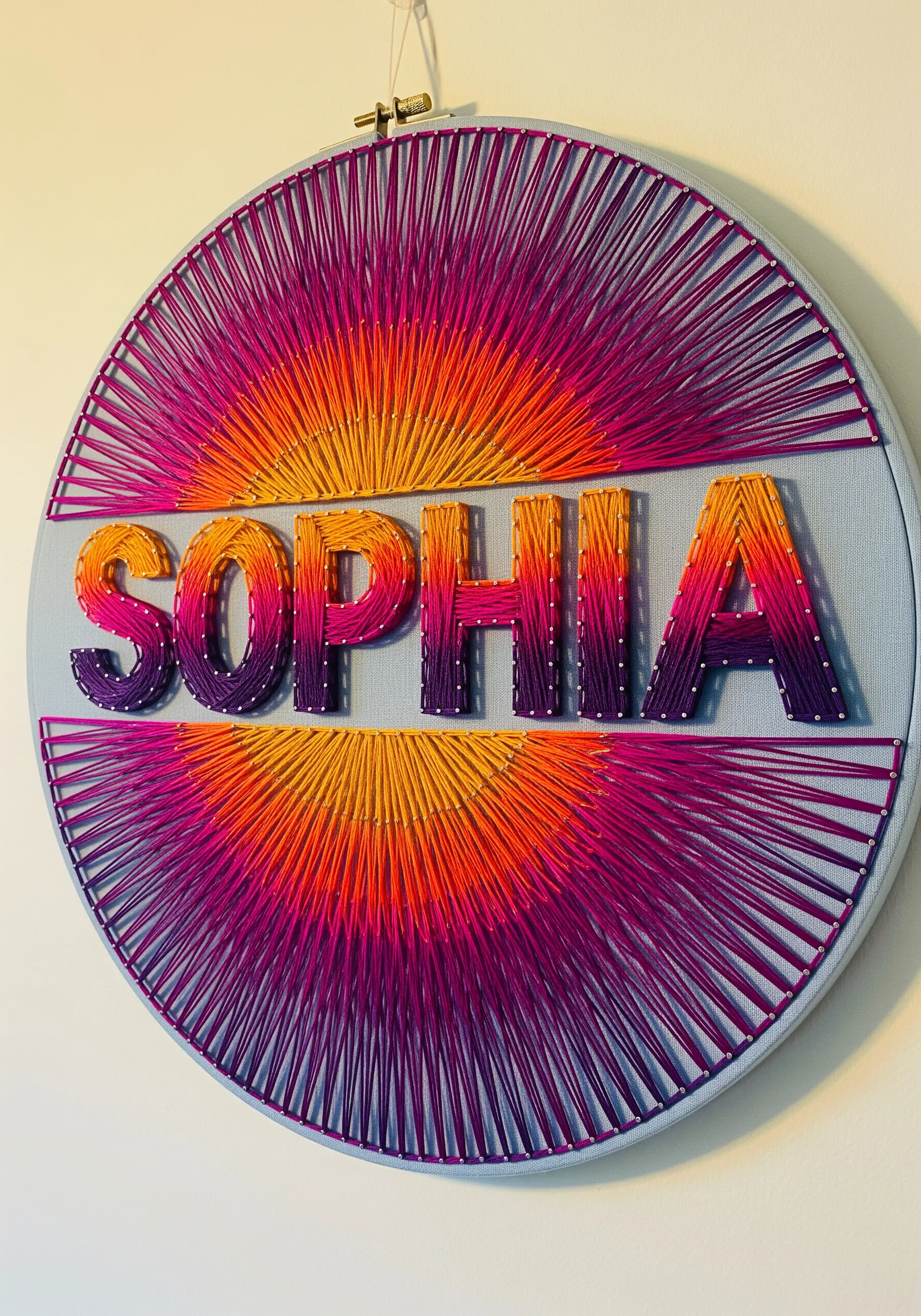 A name embroidered in a solid color over a radial sunset gradient background.