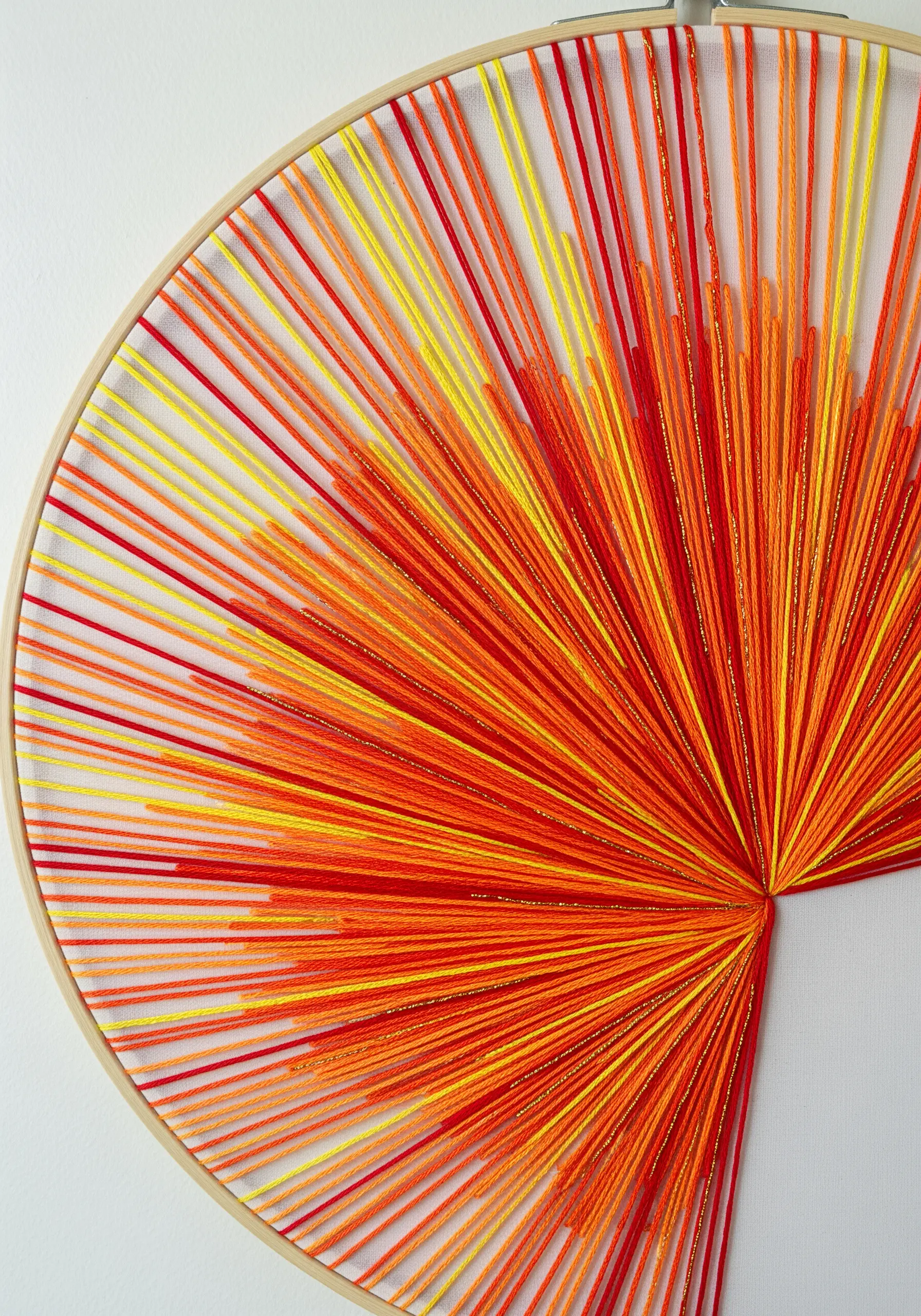 String art inside an embroidery hoop with radiating lines of red, orange, and yellow thread.