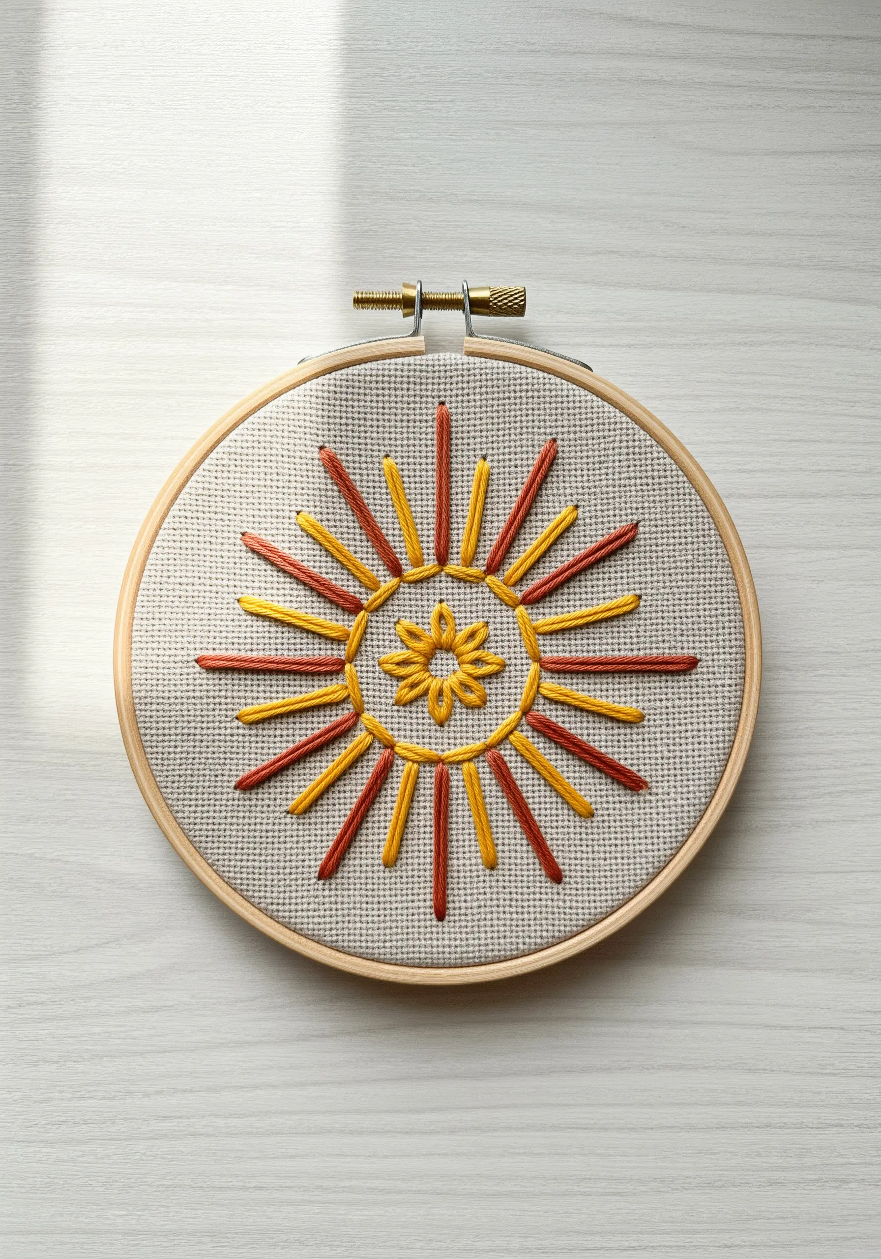 Minimalist sun mandala with orange and yellow straight stitches in a wood hoop.