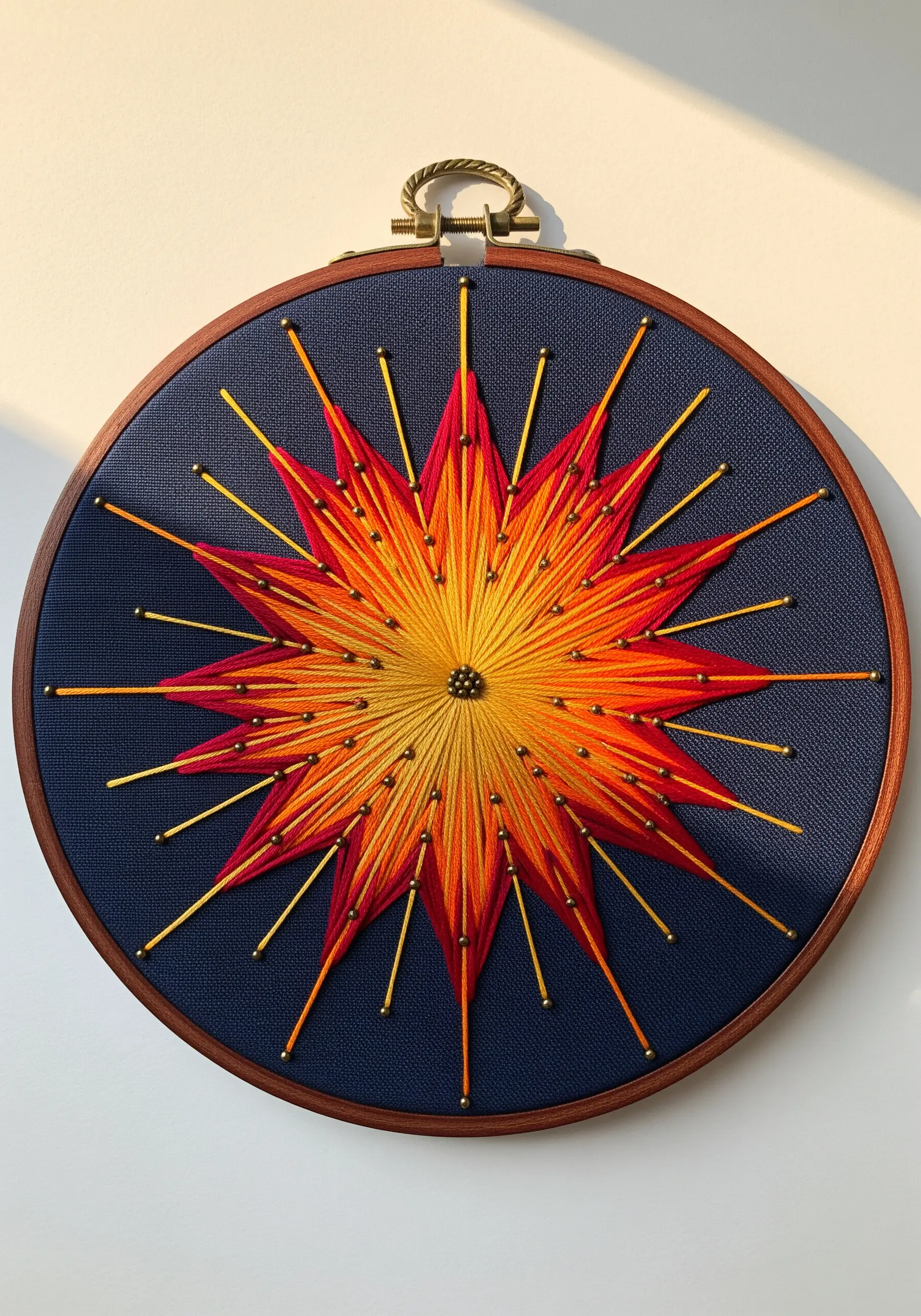 Abstract sunburst mandala with orange and red gradient satin stitch and gold beads on navy fabric.