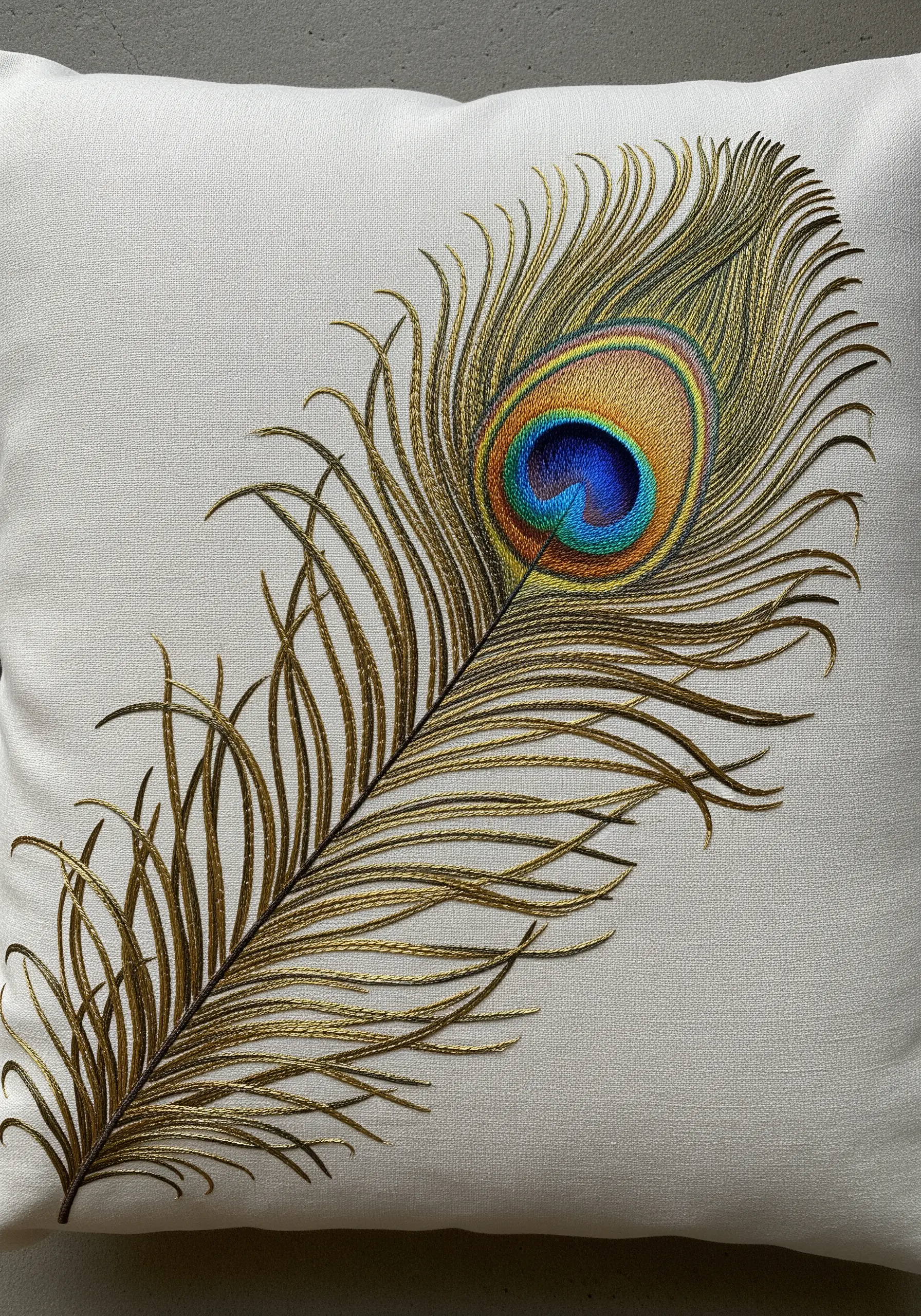 Realistic peacock feather embroidered with gold, blue, and green threads.