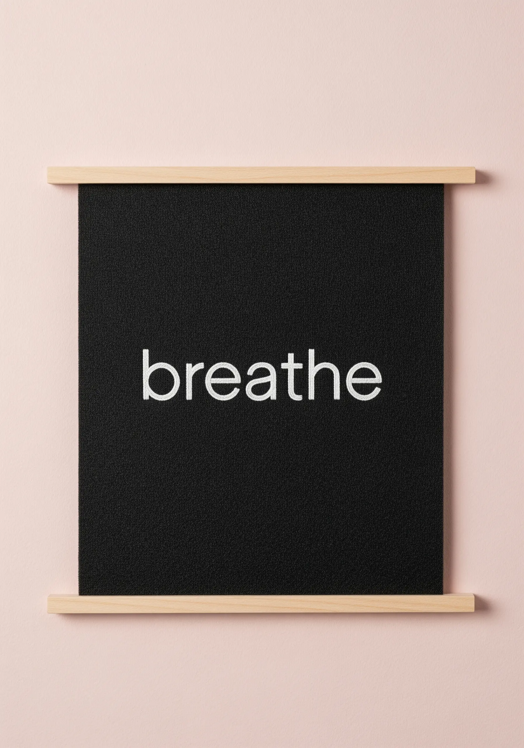 The word 'breathe' in white thread on black fabric, displayed as a wall hanging.