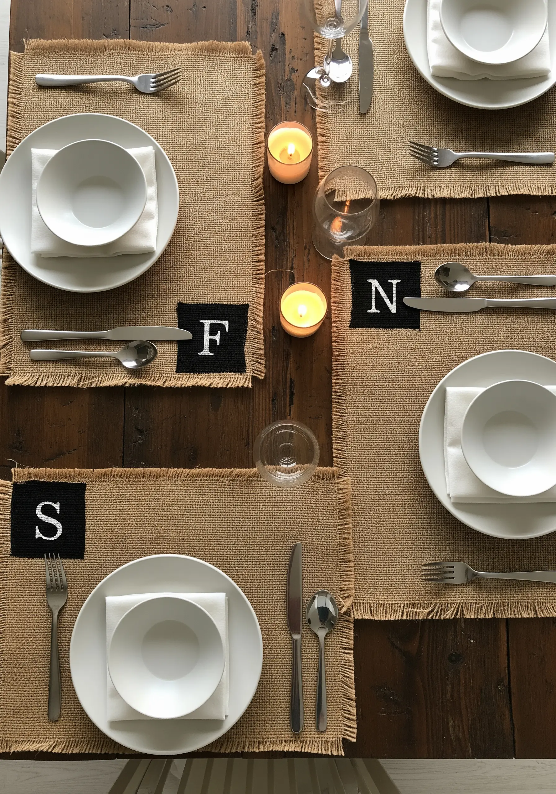 Burlap placemats on a dining table, each with a black square and white monogrammed initial.