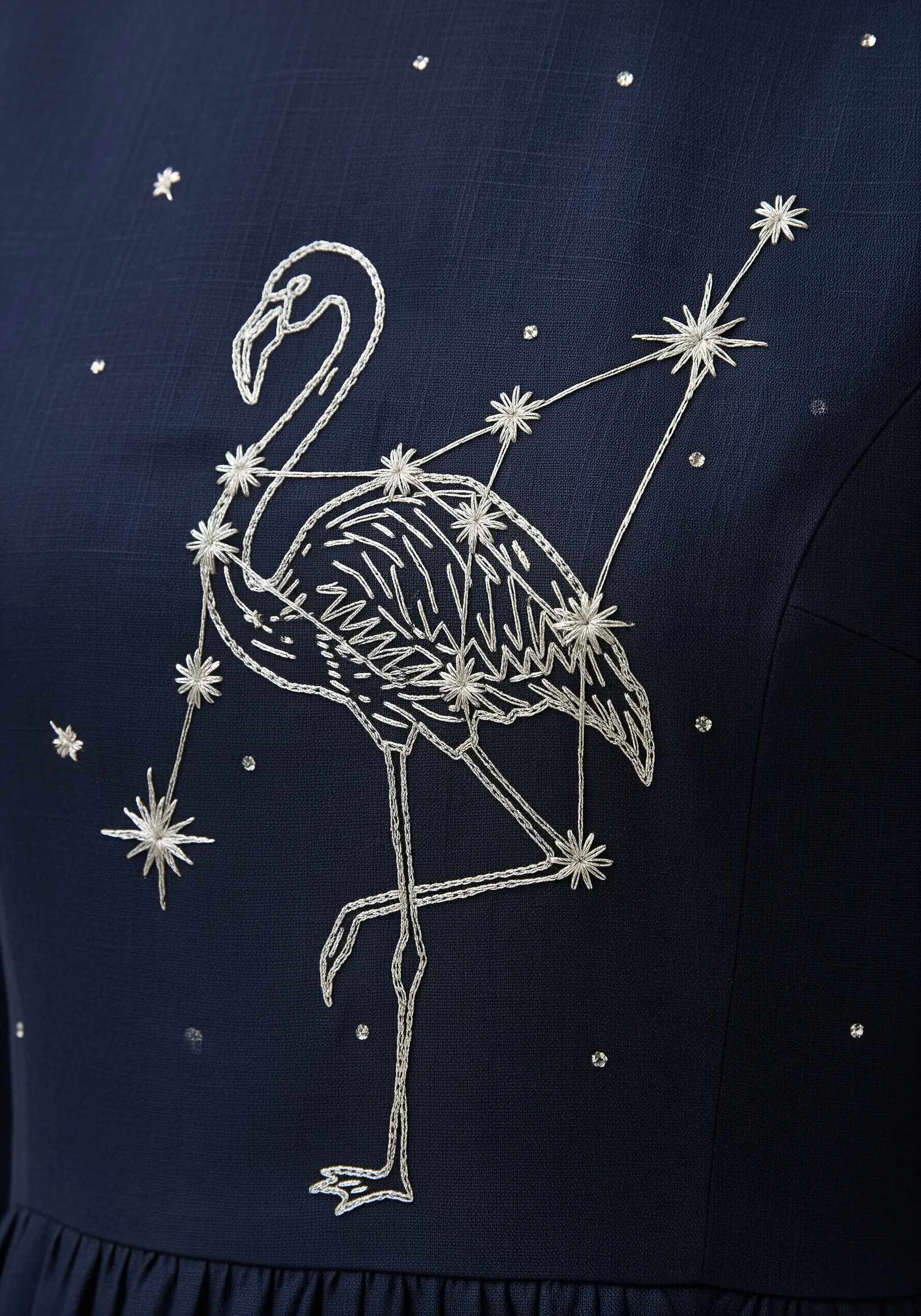 A flamingo constellation stitched in silver metallic thread on a dark navy blue dress.
