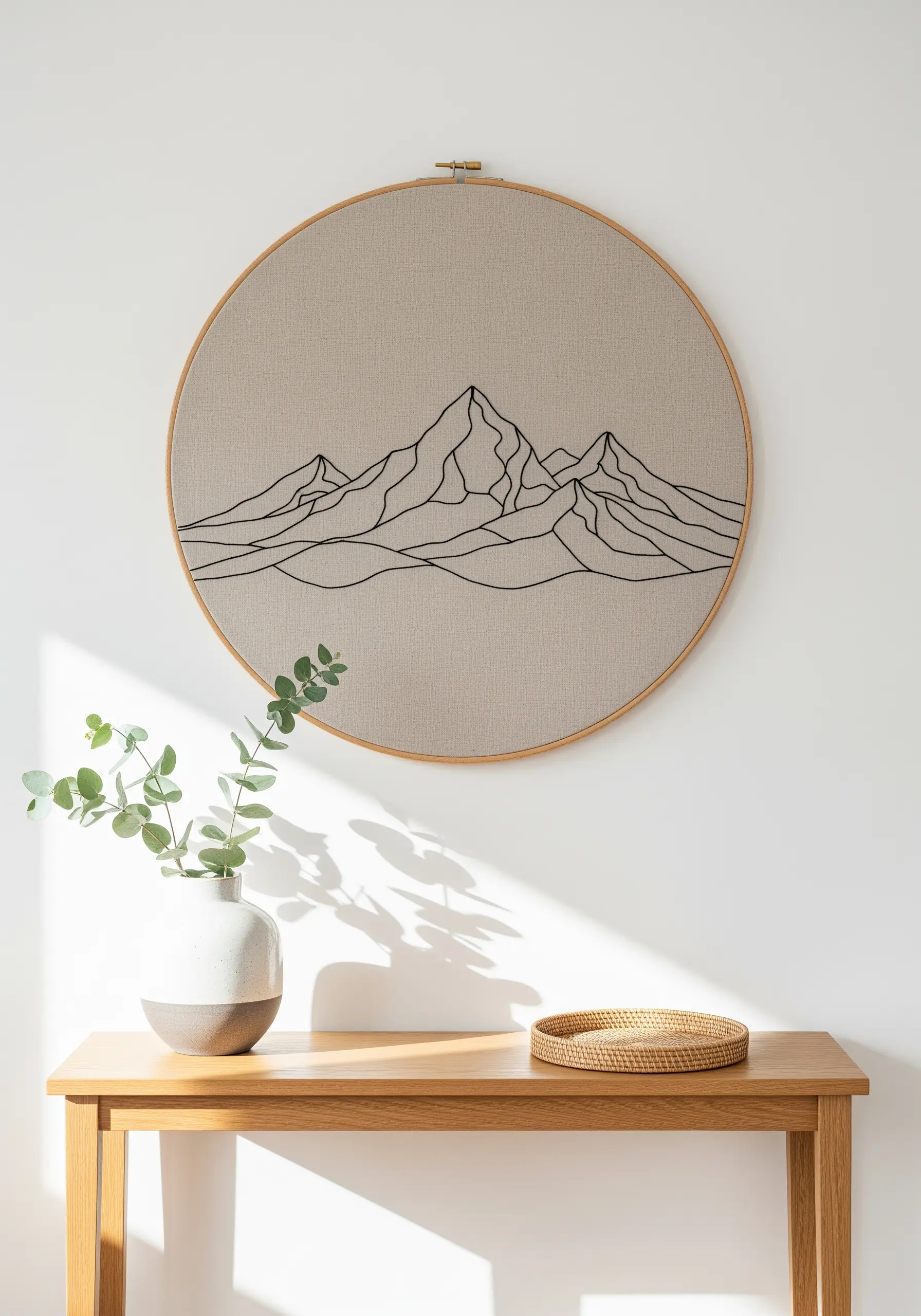 Minimalist mountain range embroidered in black thread on a large beige hoop.