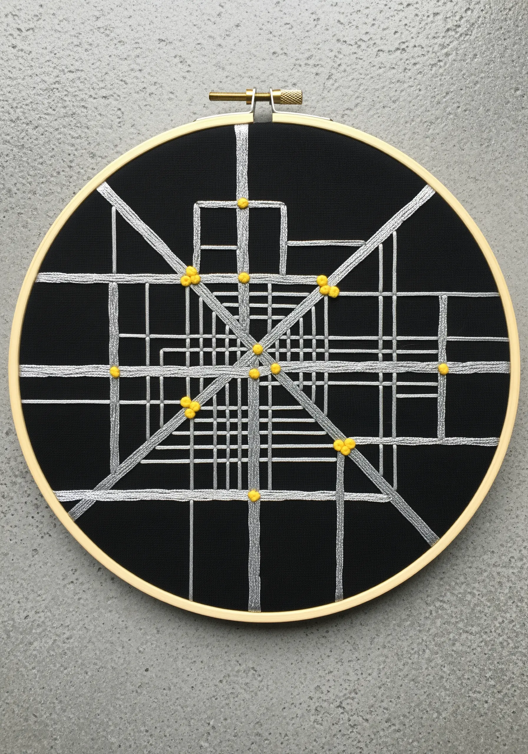 Abstract city map embroidered in silver thread with yellow French knots on black fabric.