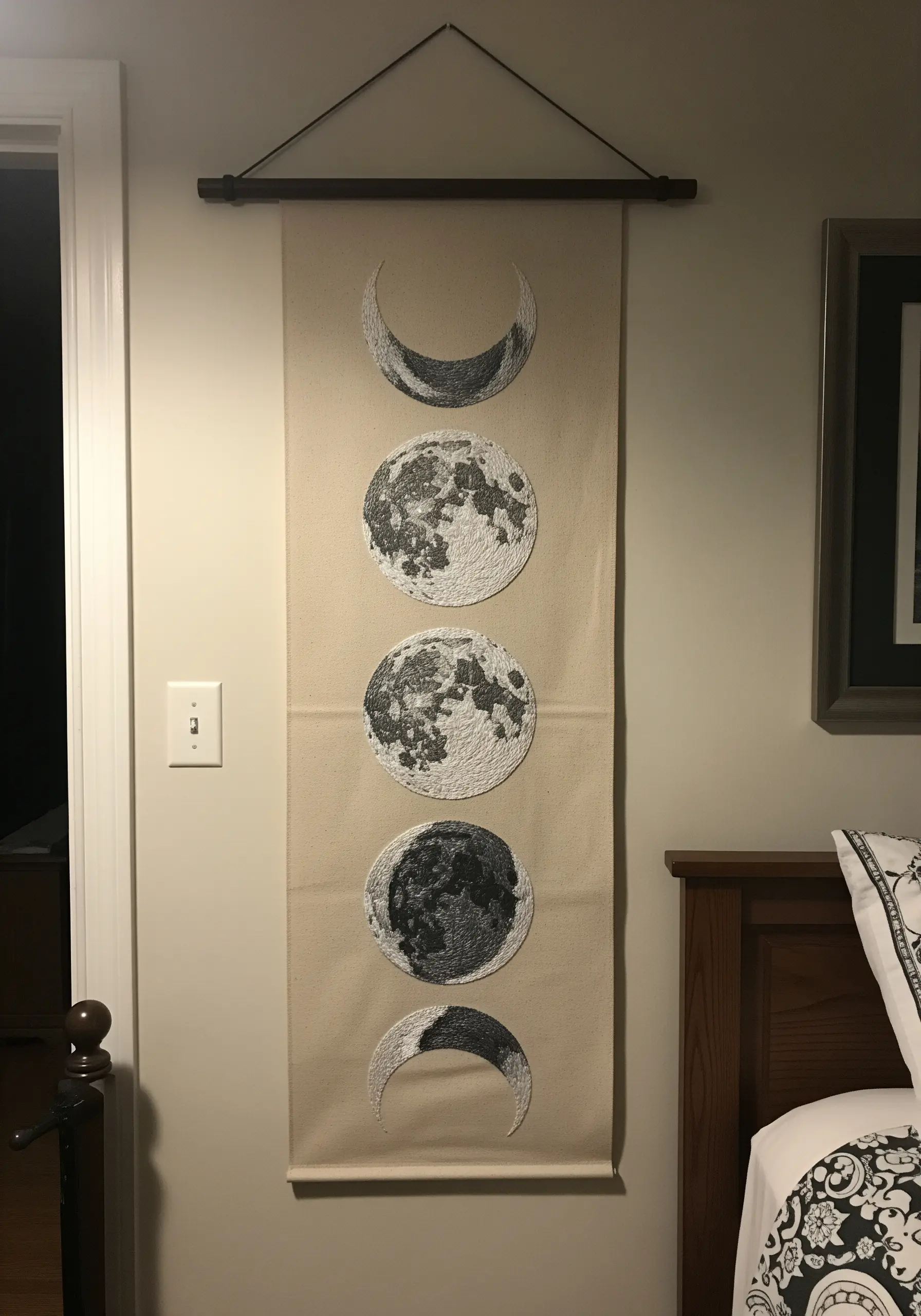 A wall hanging showing the phases of the moon, embroidered with heavy texture.