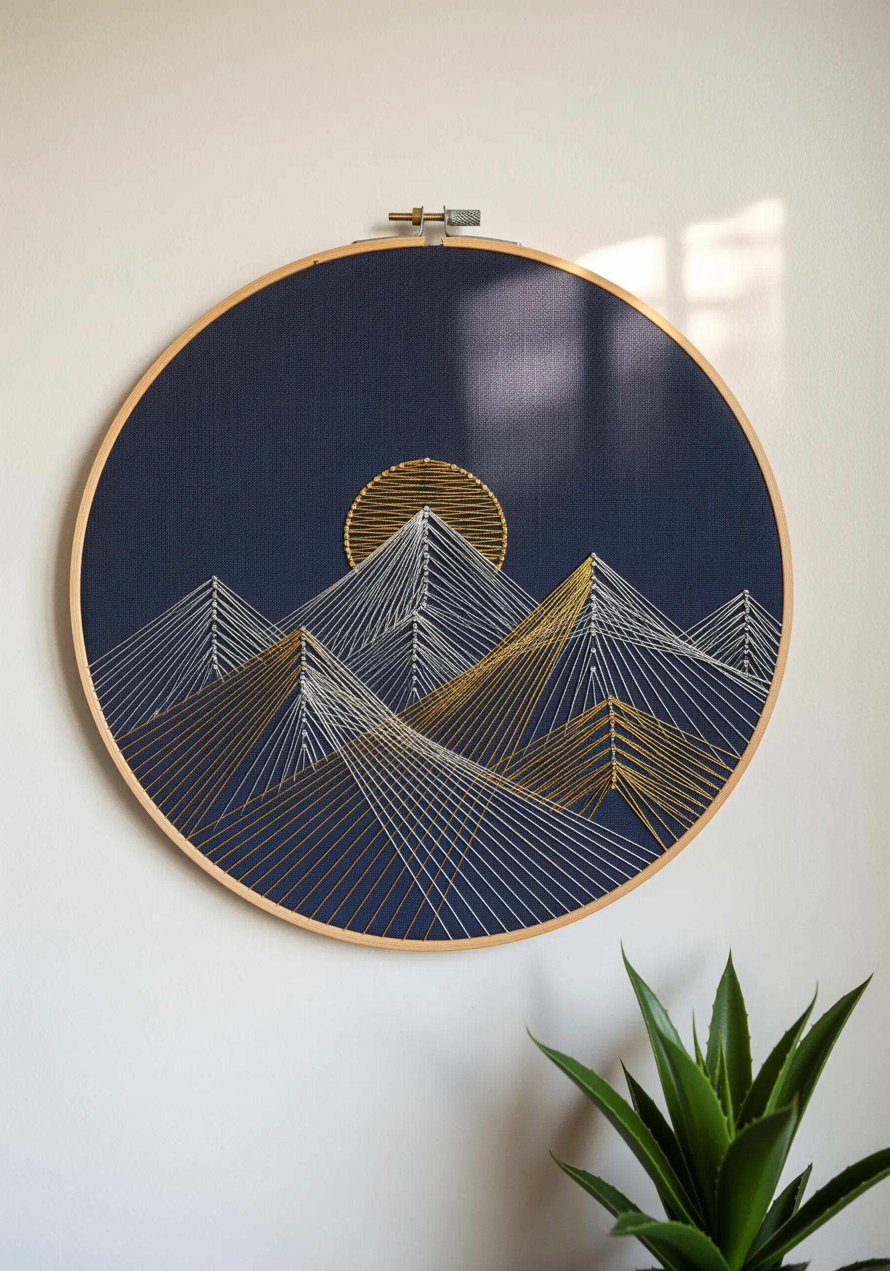 Geometric mountain range embroidered with gold and white thread on dark navy fabric in a hoop.