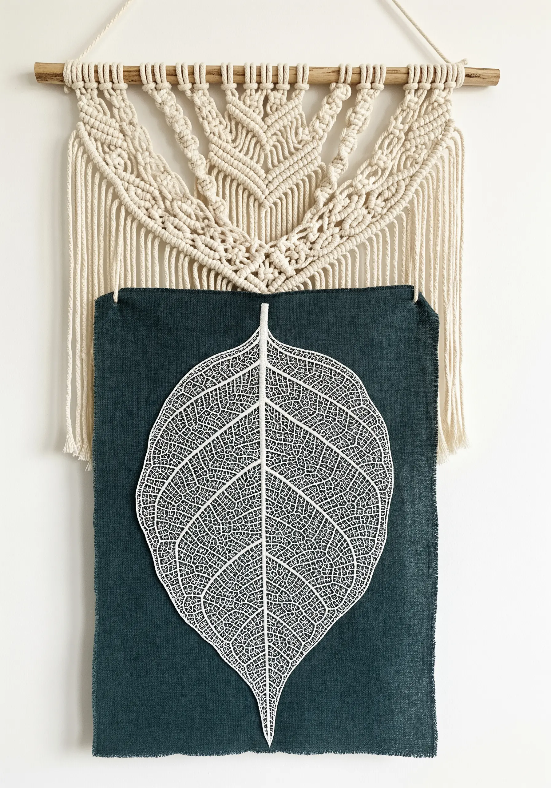 A delicate white skeleton leaf mounted on dark teal fabric with a macrame hanger.