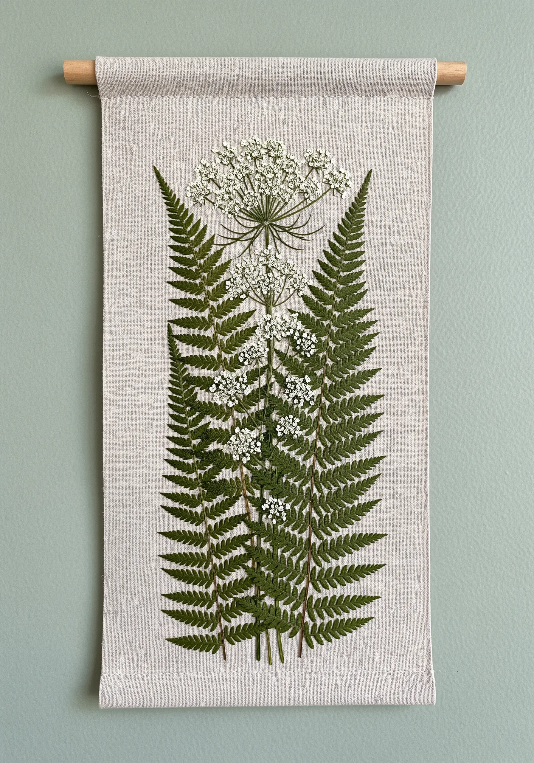 A wall hanging featuring realistic pressed ferns and Queen Anne's lace on canvas.