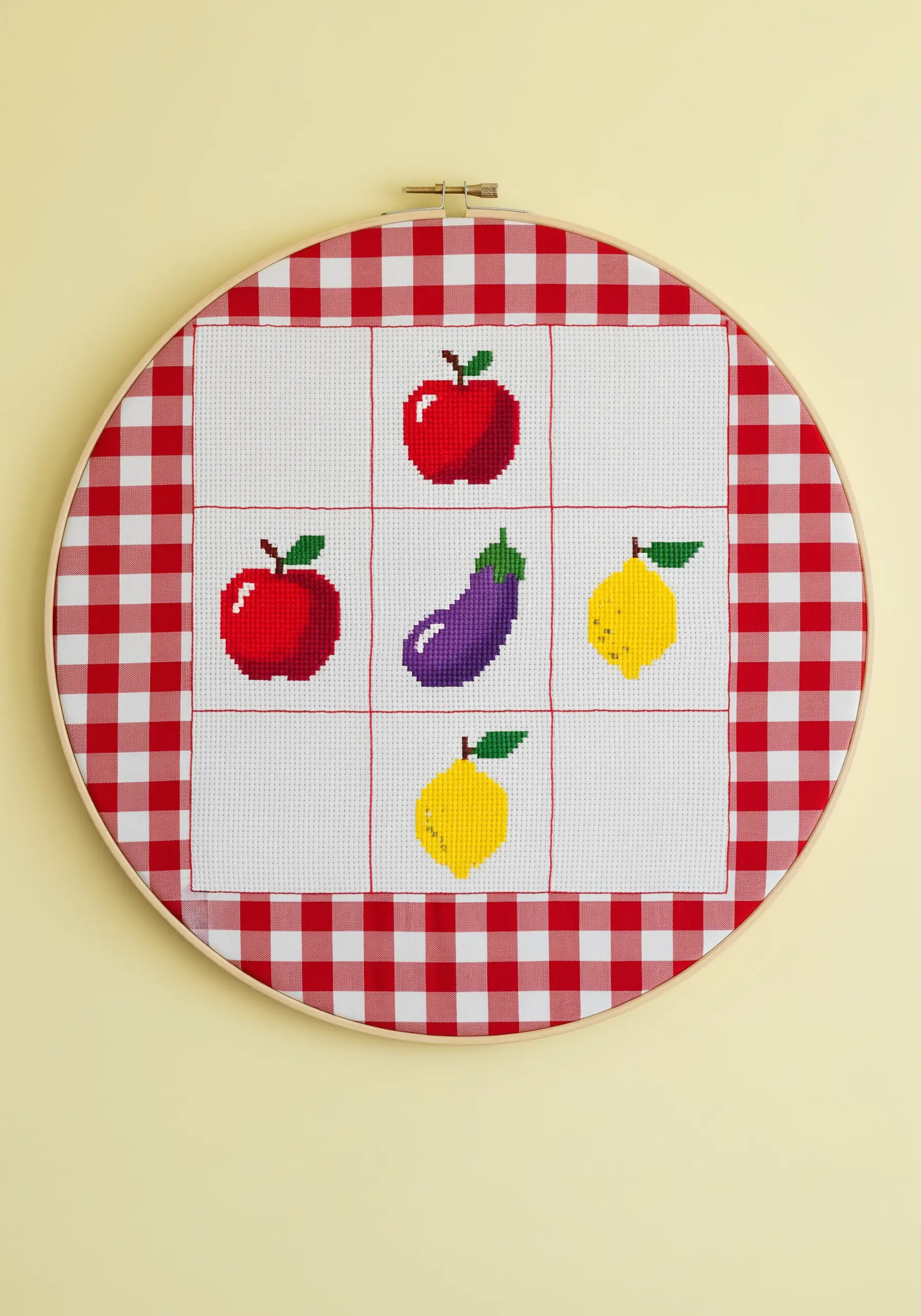 Cross-stitched fruit motifs on a red-and-white gingham fabric in an embroidery hoop.