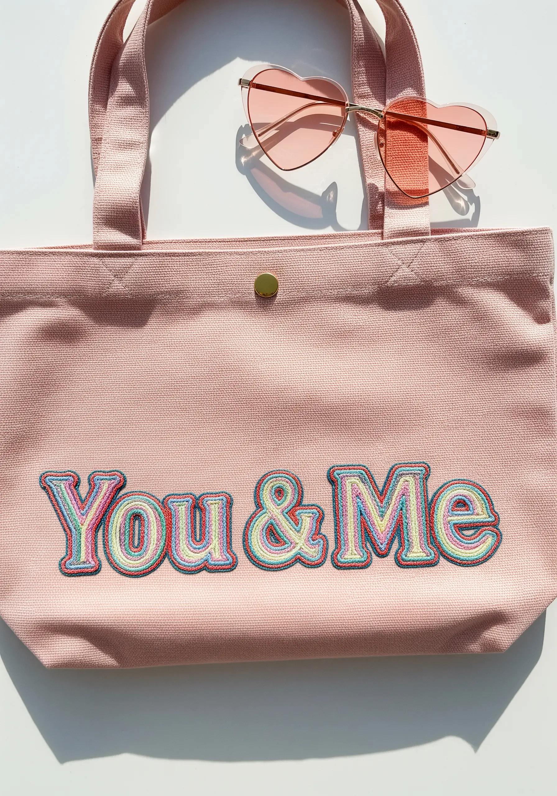 The words 'You & Me' embroidered in a colorful, layered retro font on a pink canvas tote bag.