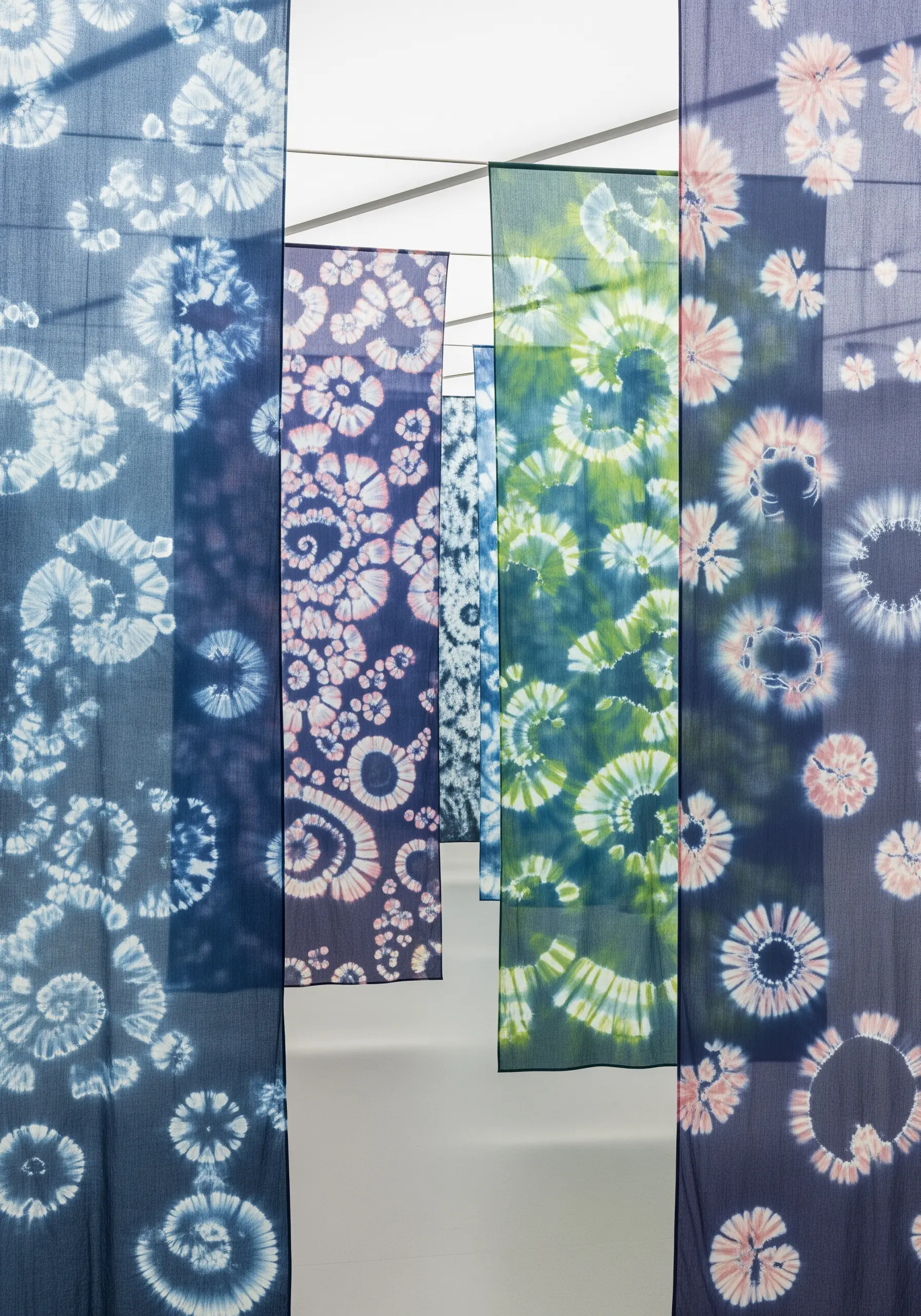 Hanging panels of indigo fabric with circular and floral tie-dye patterns.